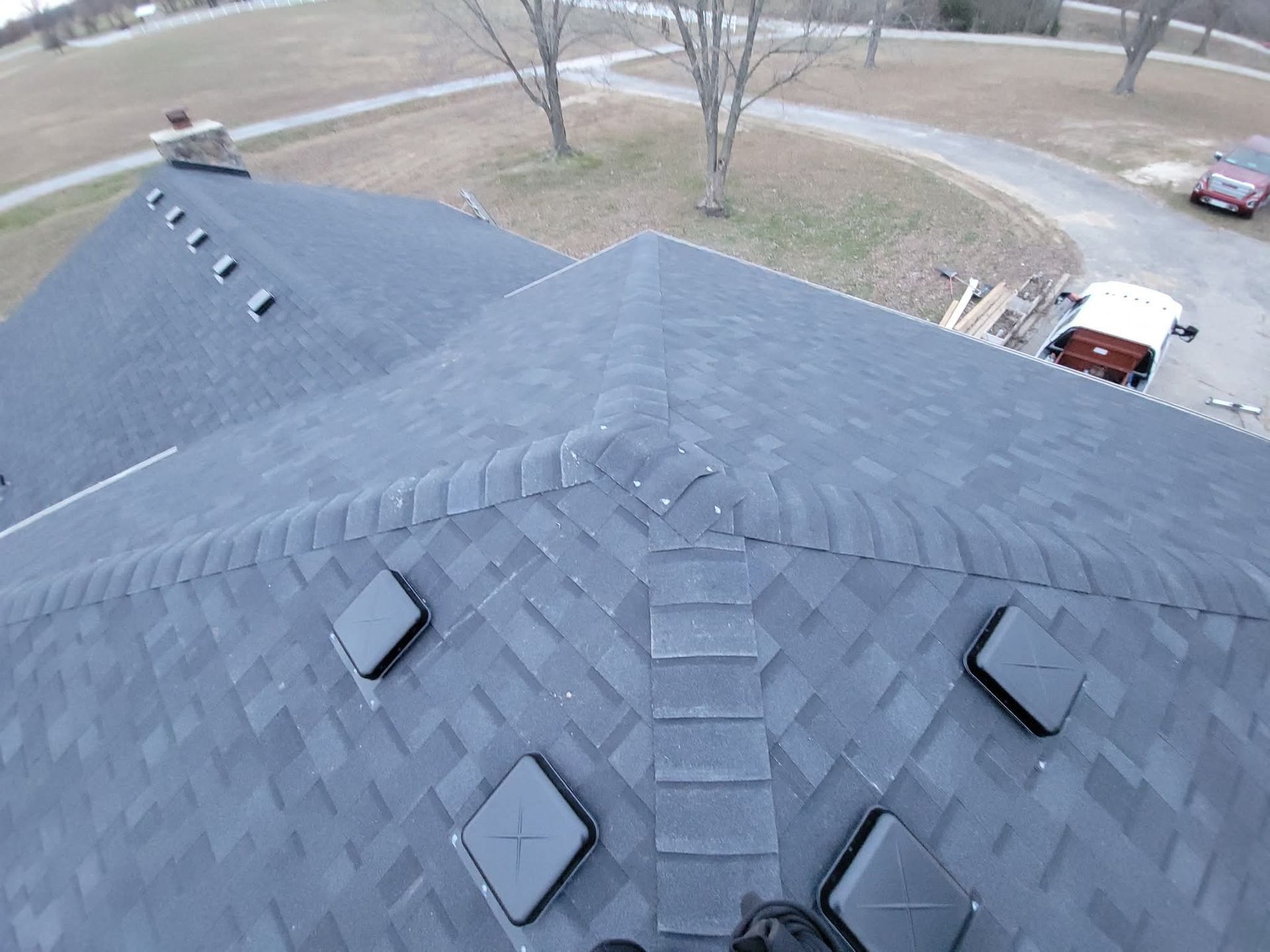 Dark gray shingle roof with square vents. The roof is on a house in an outdoor setting.