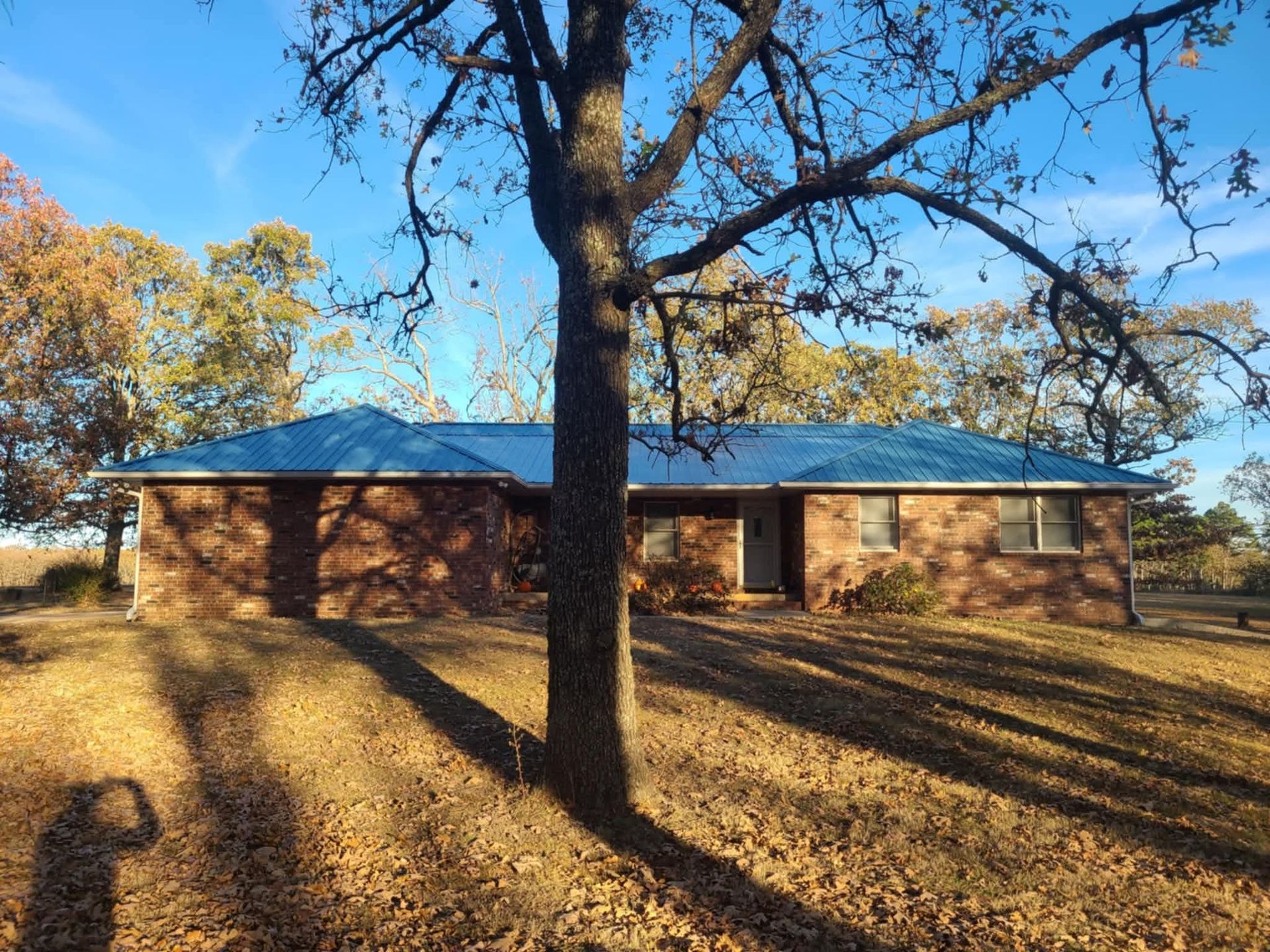 Brick house with blue roof, autumn trees, and sunlight casting shadows.