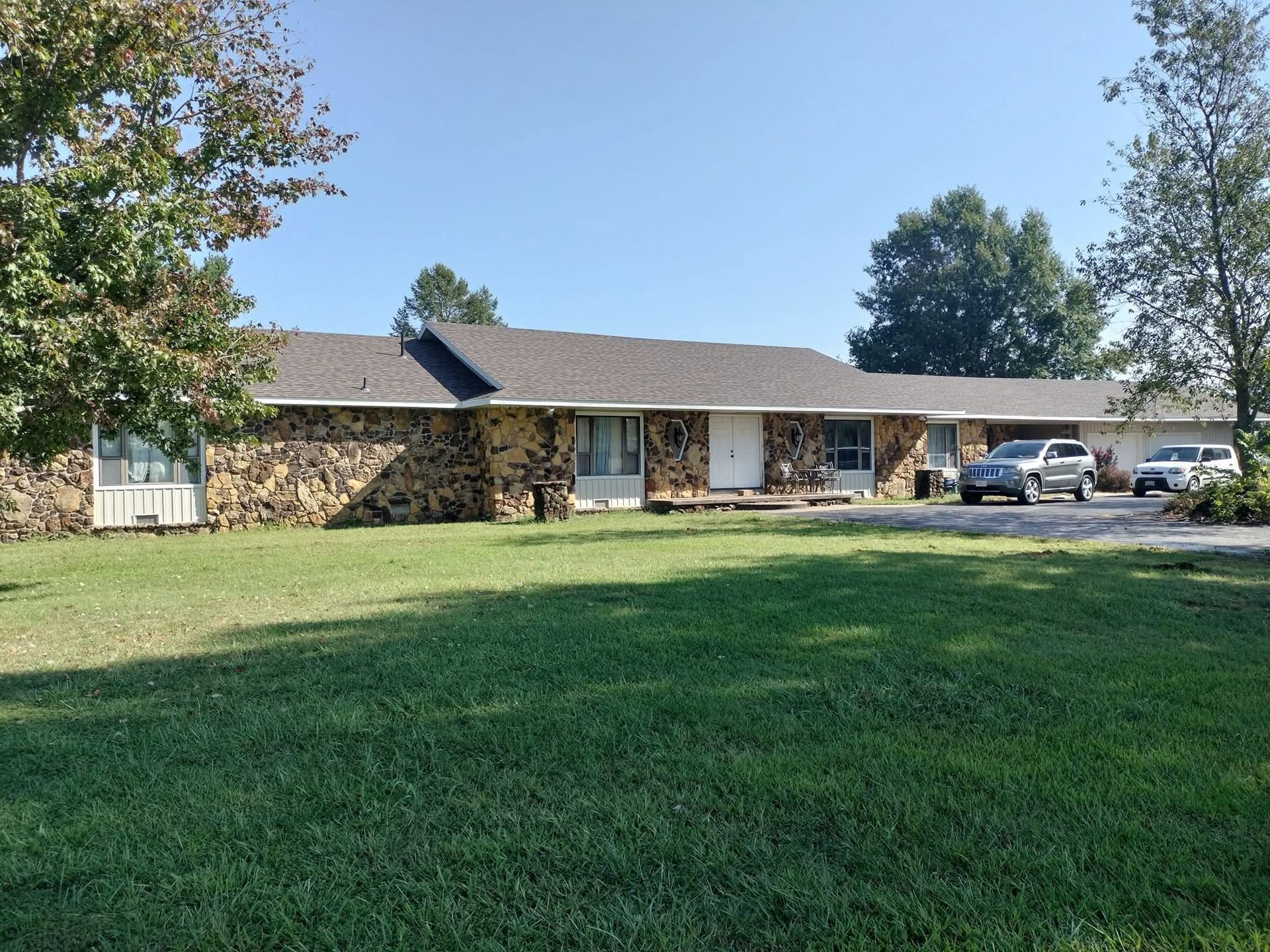 Single-story building with textured stone exterior and dark roof; cars parked in front on a sunny day.