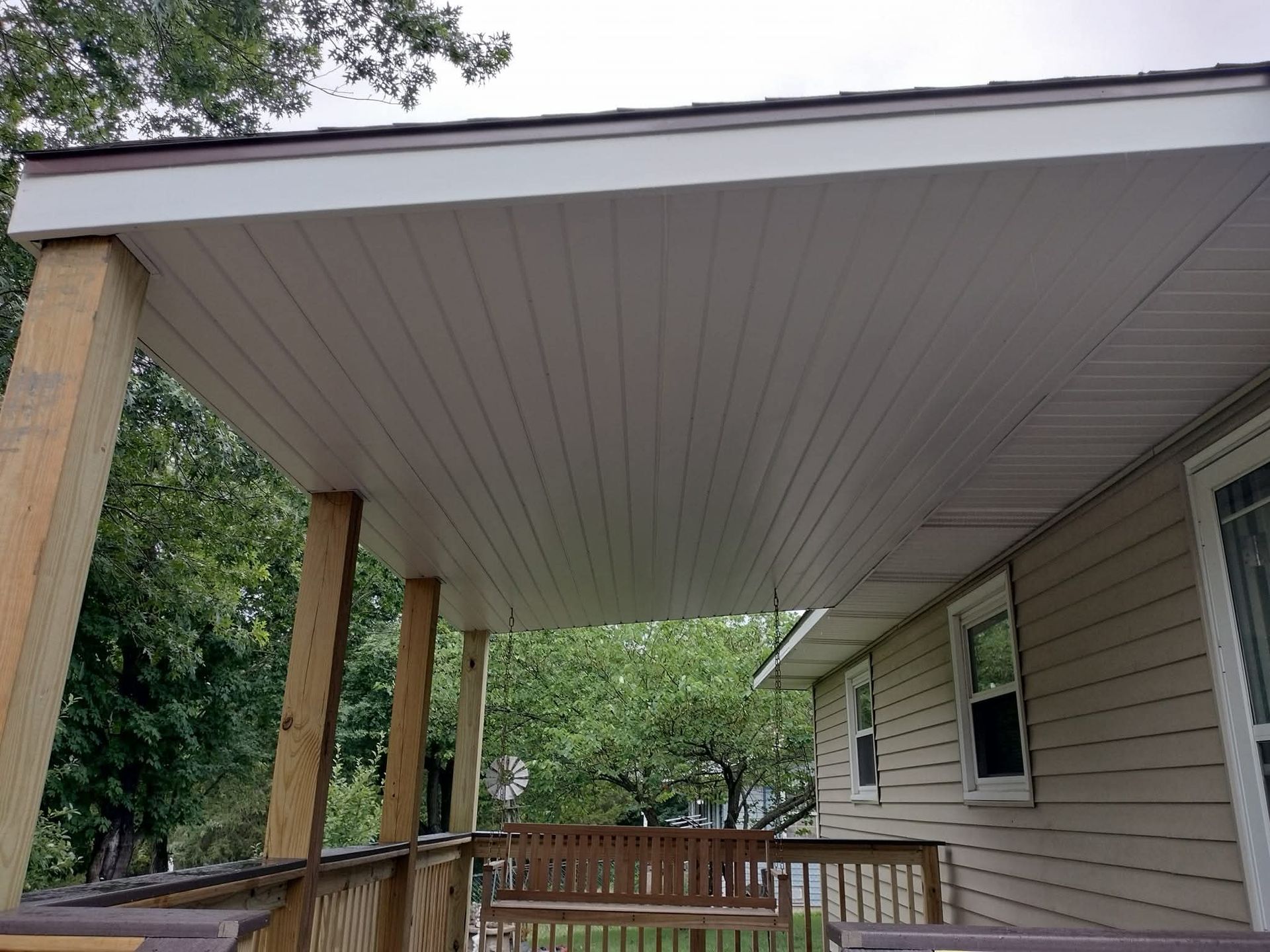 Covered porch with light brown siding, wooden posts, and a swing.