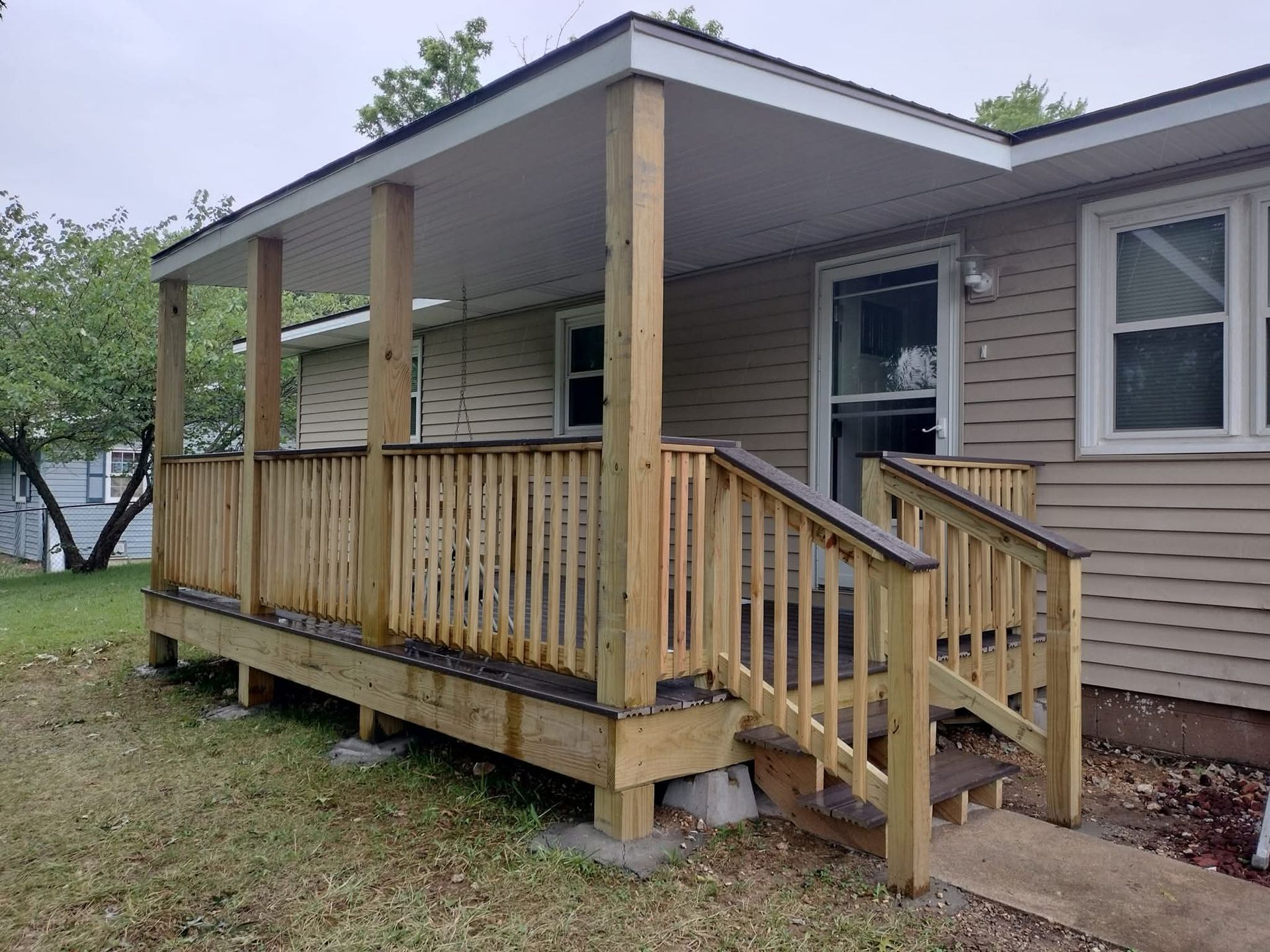 Wooden porch with railing and roof attached to a beige house, cloudy day.