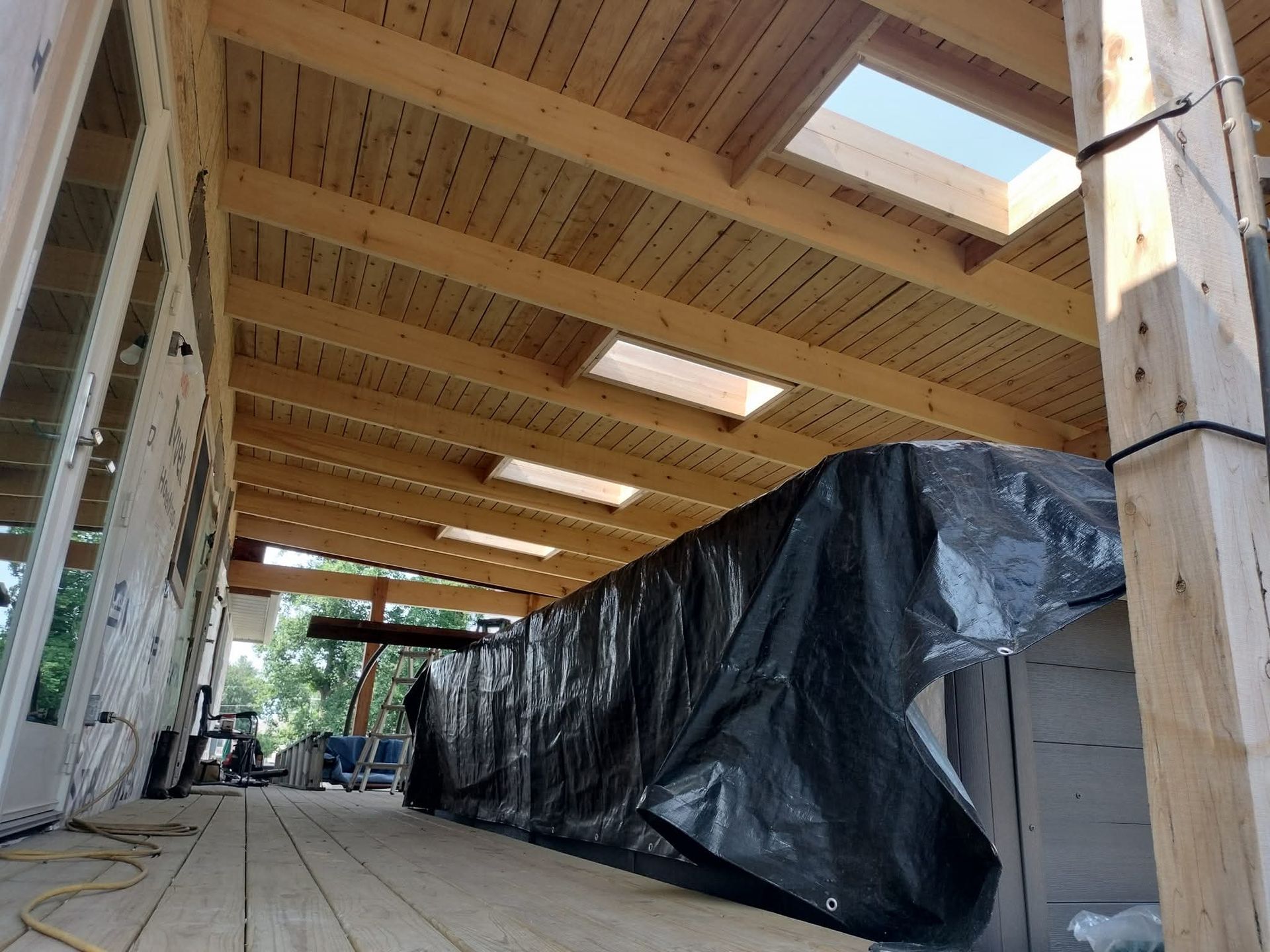 Wooden structure with skylights, under construction. Covered object in the center, and a wooden deck.
