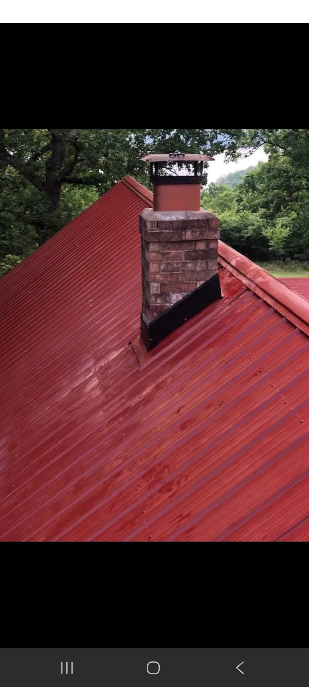Red corrugated metal roof with brick chimney, trees in background.