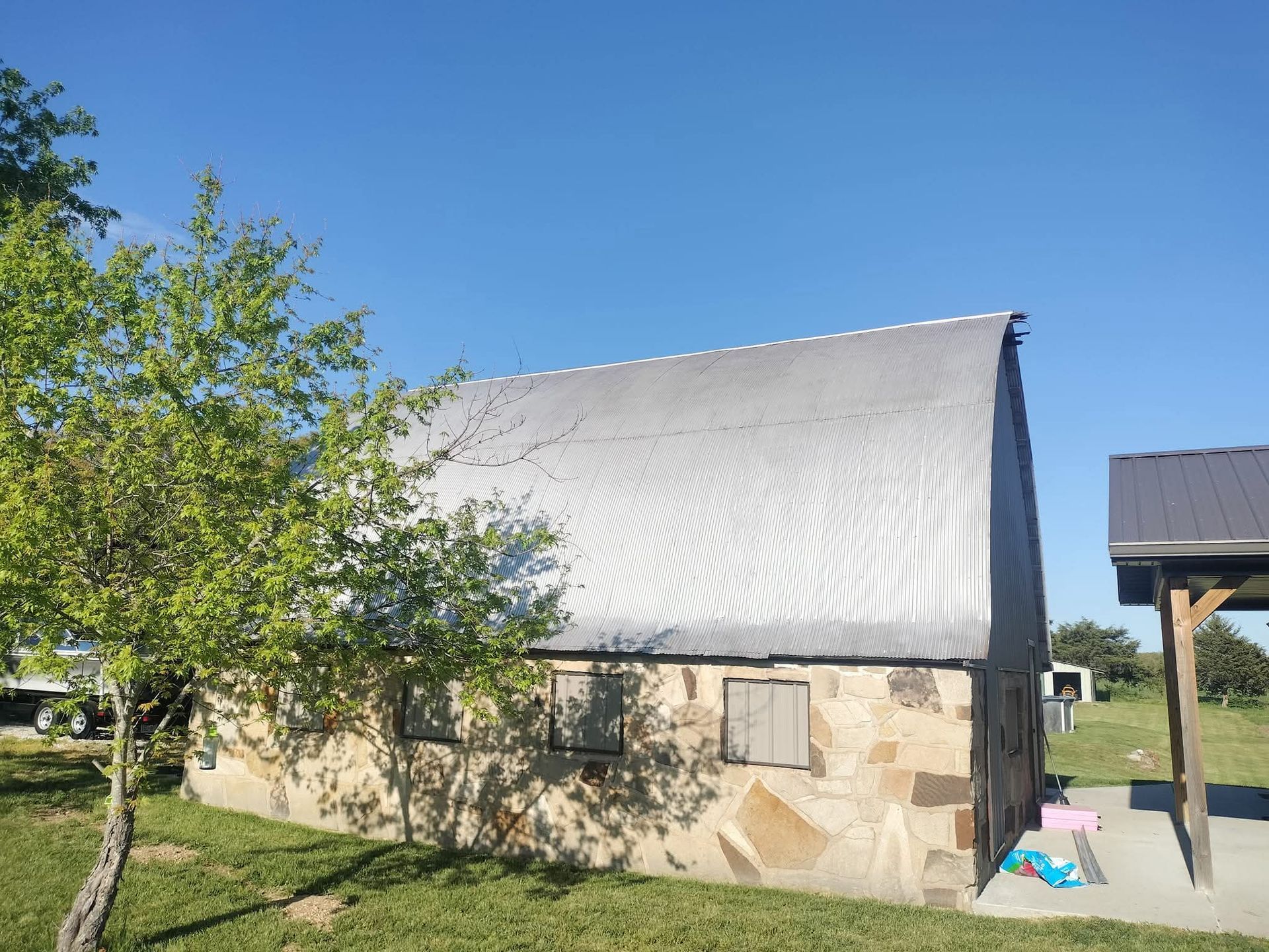 Stone building with corrugated metal roof, tree in front, sunny day.