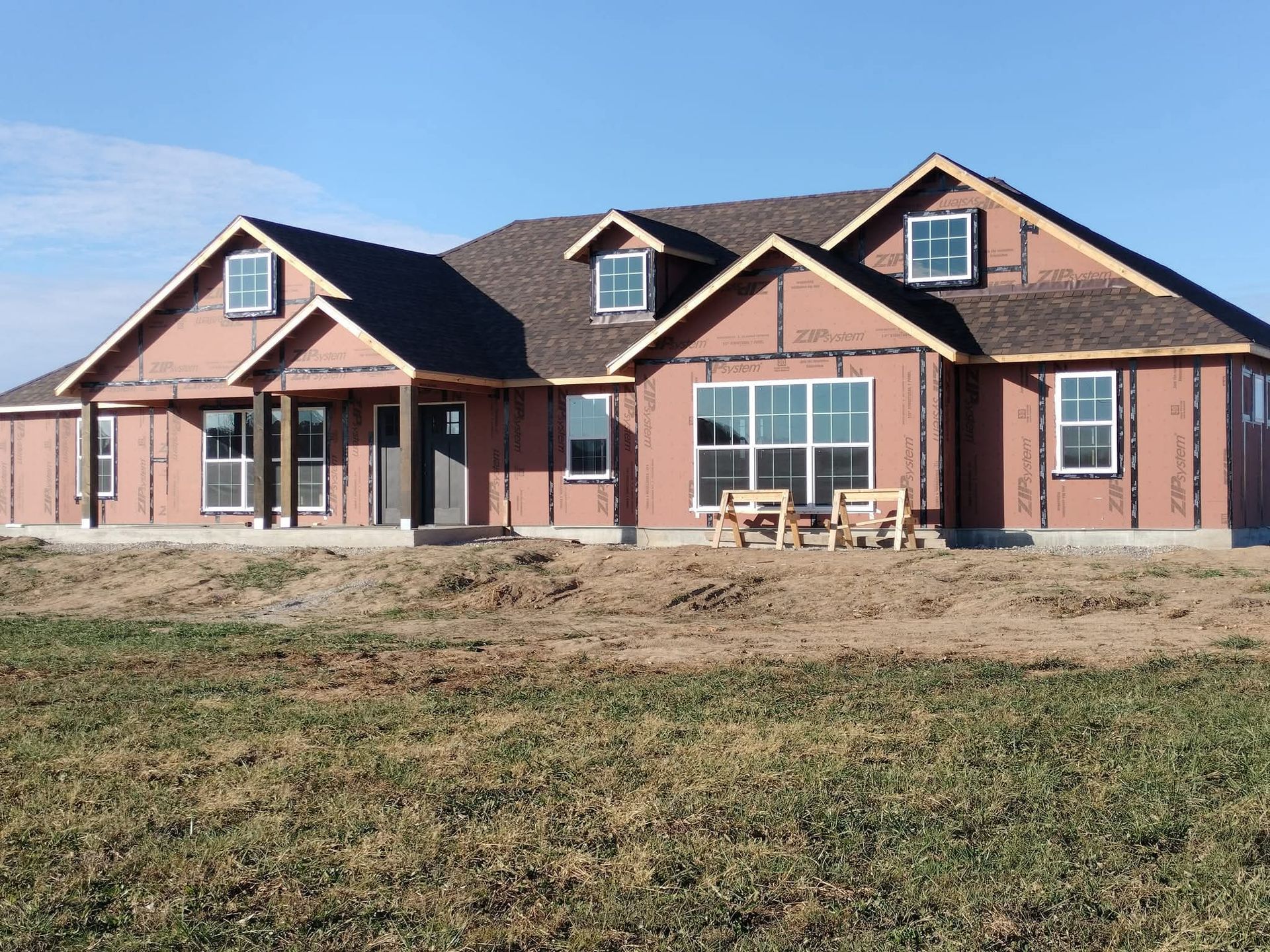 House under construction; brown siding, dark roof, windows, dormers, and blue sky.