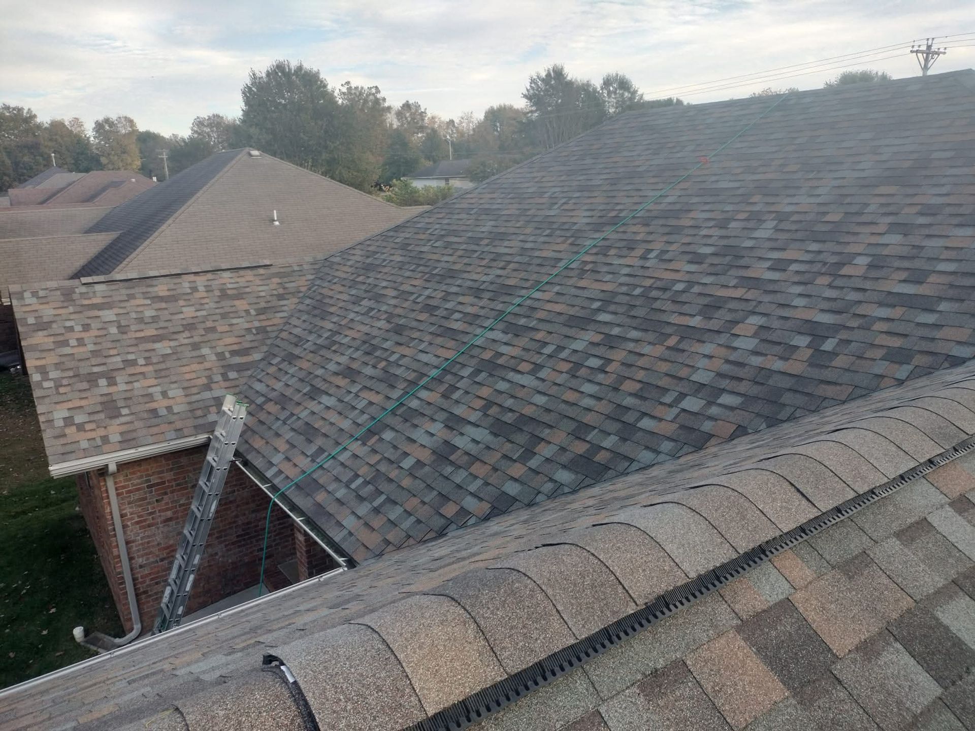 Overhead view of several asphalt shingle roofs on houses. Brown and grey shingles, overcast sky.