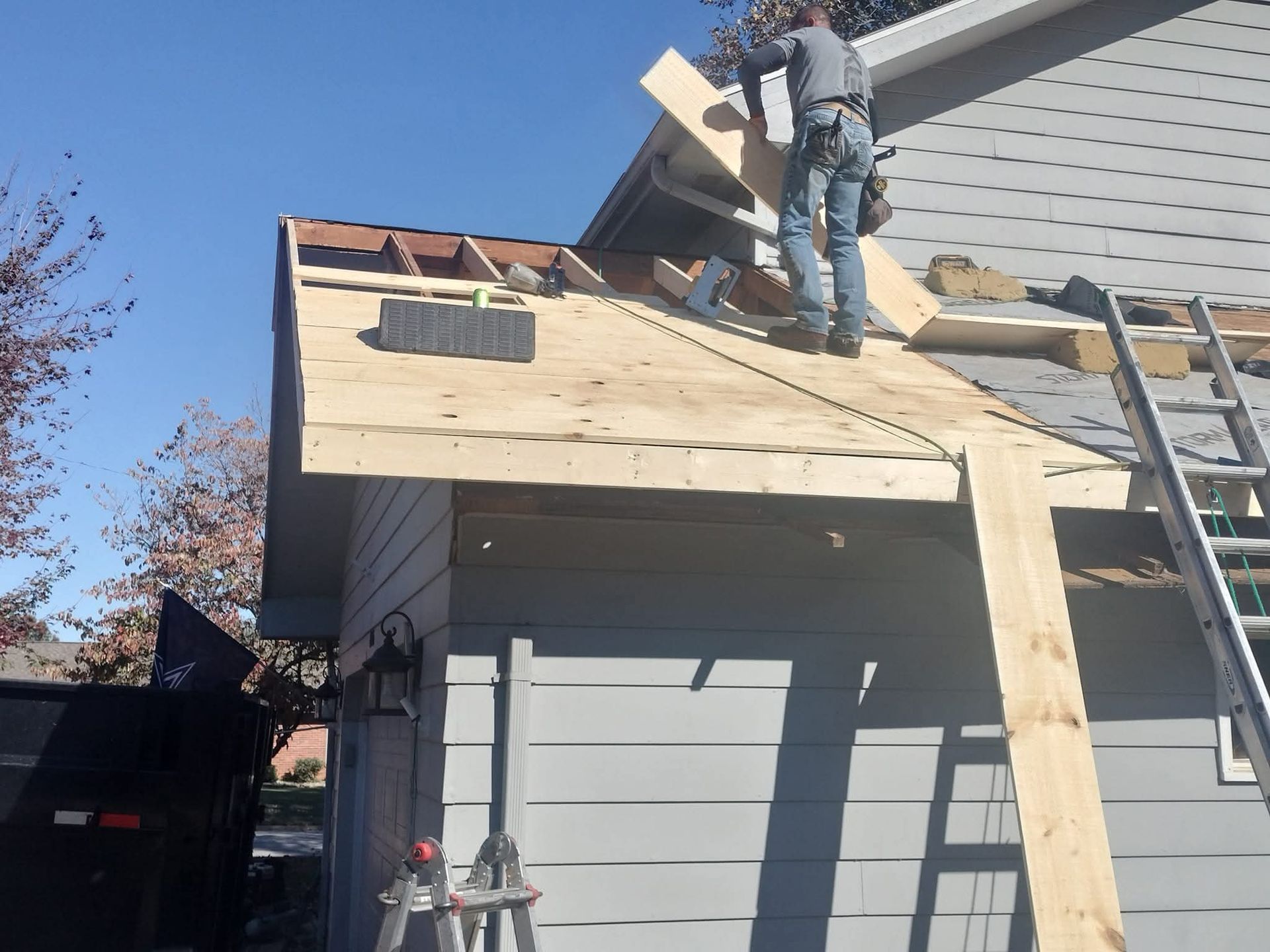 Construction worker on a roof installing wood. A ladder is present. Bright, sunny day.
