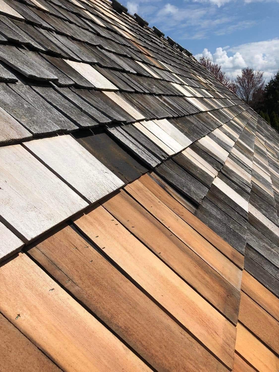 Wooden shingle roof with varied colors: light tan, brown, gray, and white, under a blue sky.