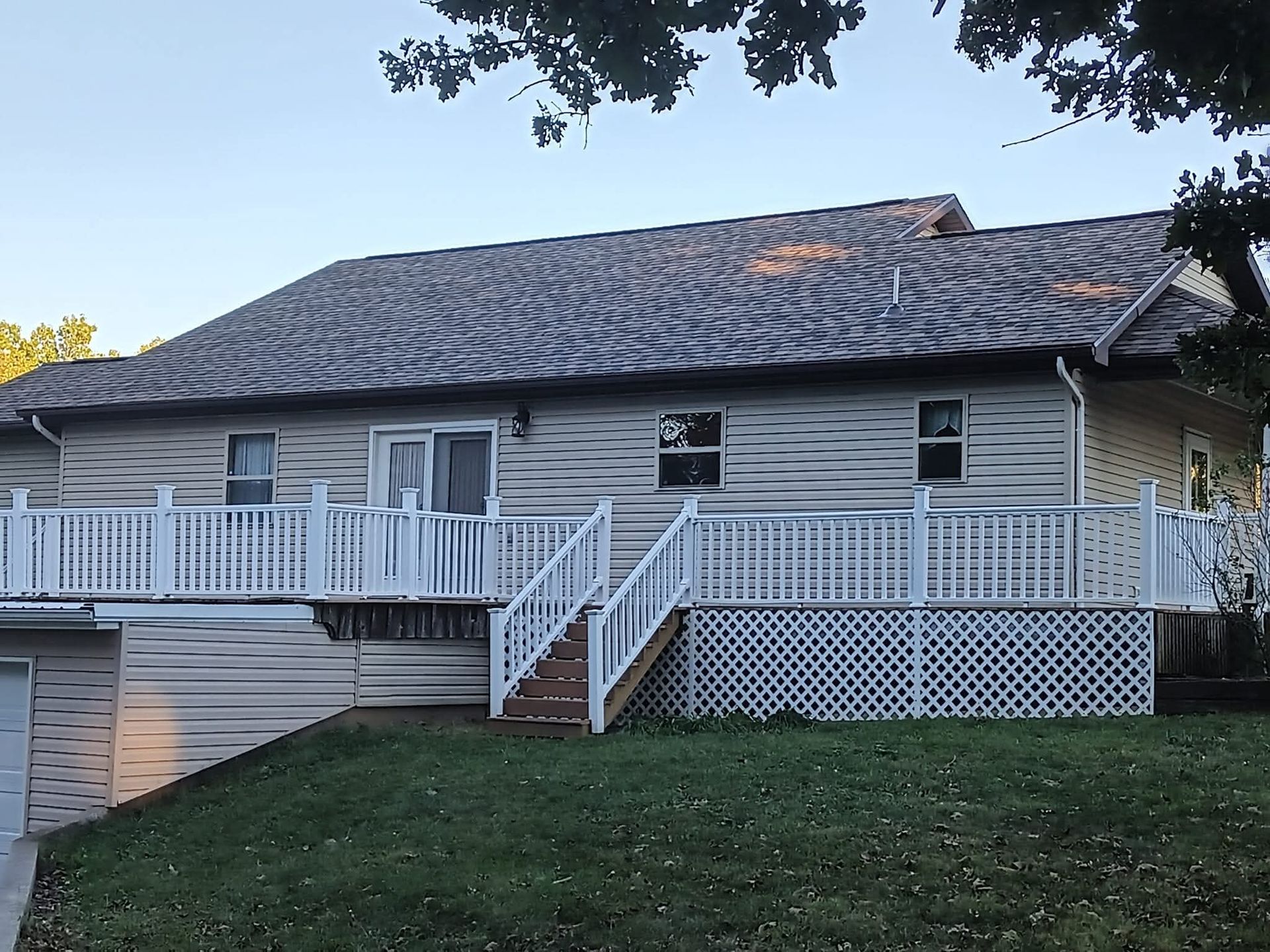 Beige house with a large deck, white railings, and a gray roof; green grass in front.