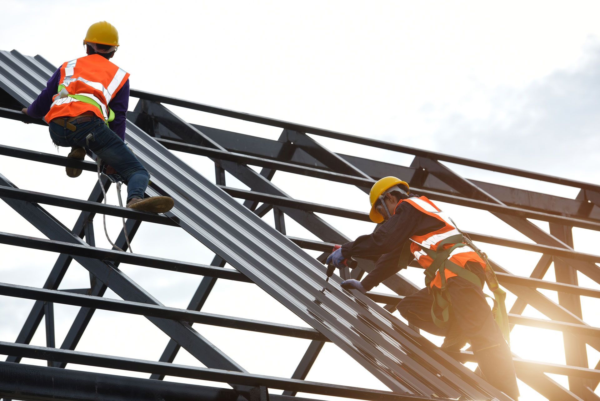 Construction workers installing metal roofing on a framework, wearing safety vests and helmets.