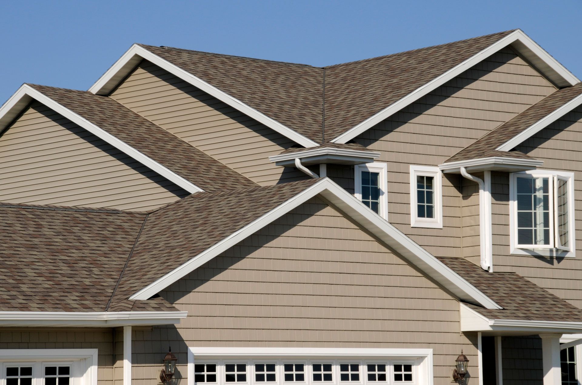 Tan house with complex roofline, white trim, blue sky.