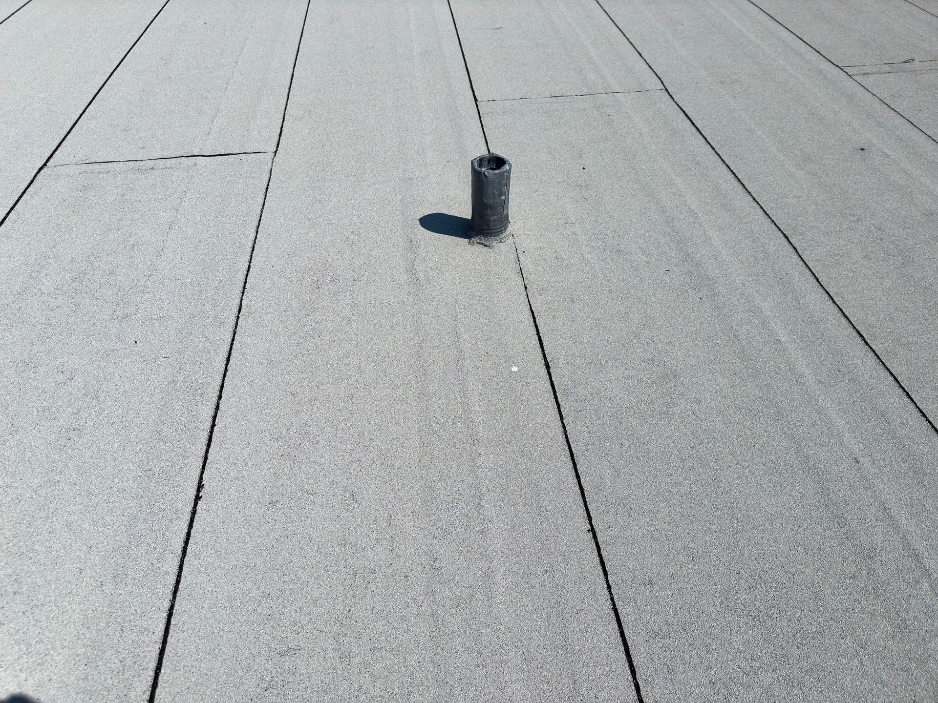 Gray flat roof with a cylindrical vent pipe.