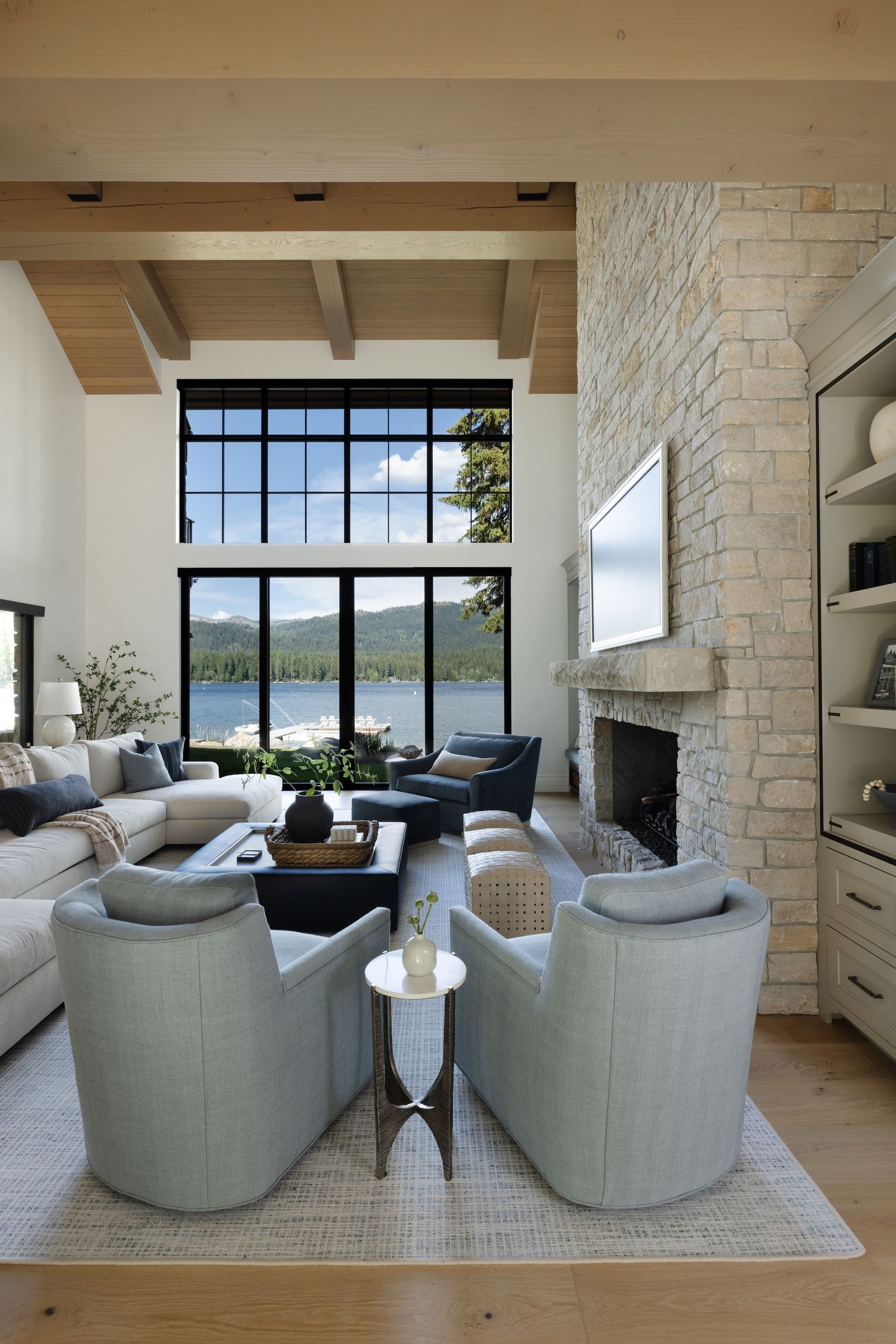 Bright living room with high windows, stone fireplace, and two gray chairs facing a mountain view