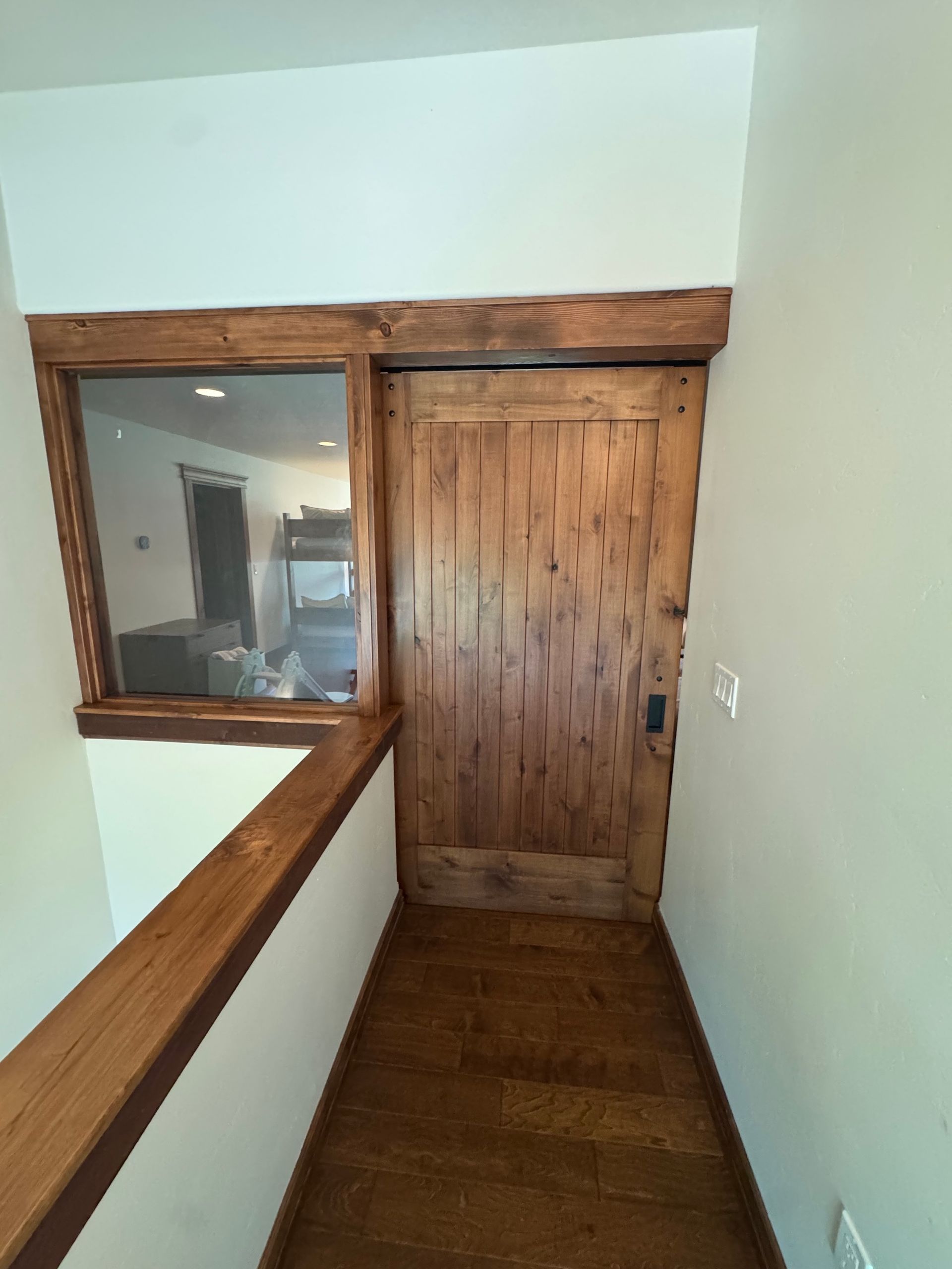 Narrow hallway with wood trim, a wooden door, and a pass-through window into another room.