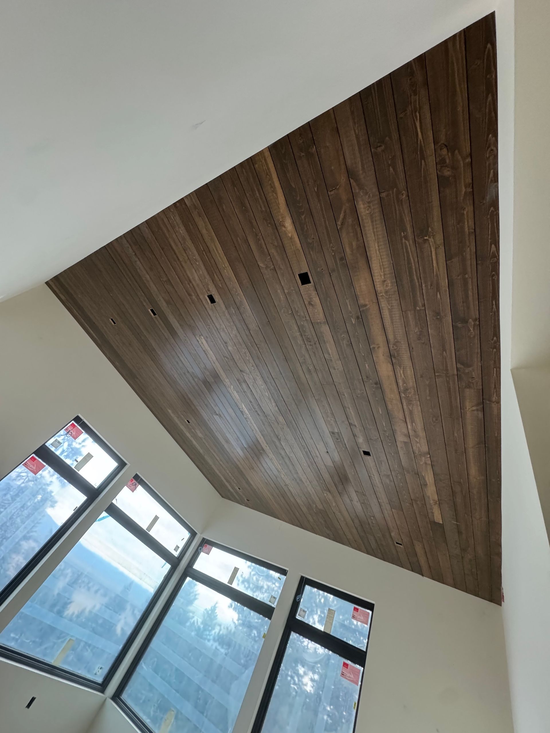 Wood-paneled cathedral ceiling above tall windows in a bright room