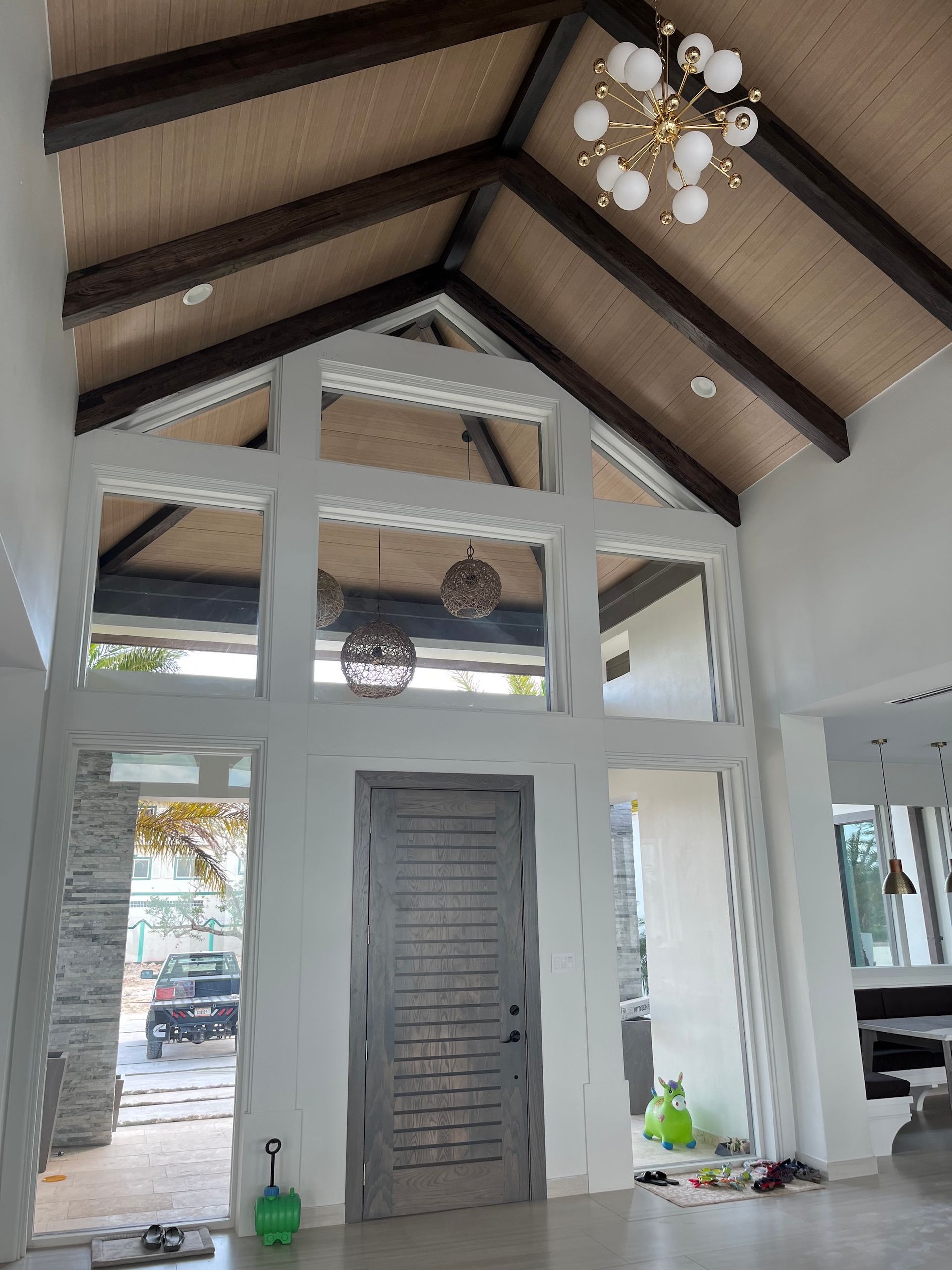 Indoor entry hall with vaulted wood ceiling, gray front door, and white-framed windows and columns.