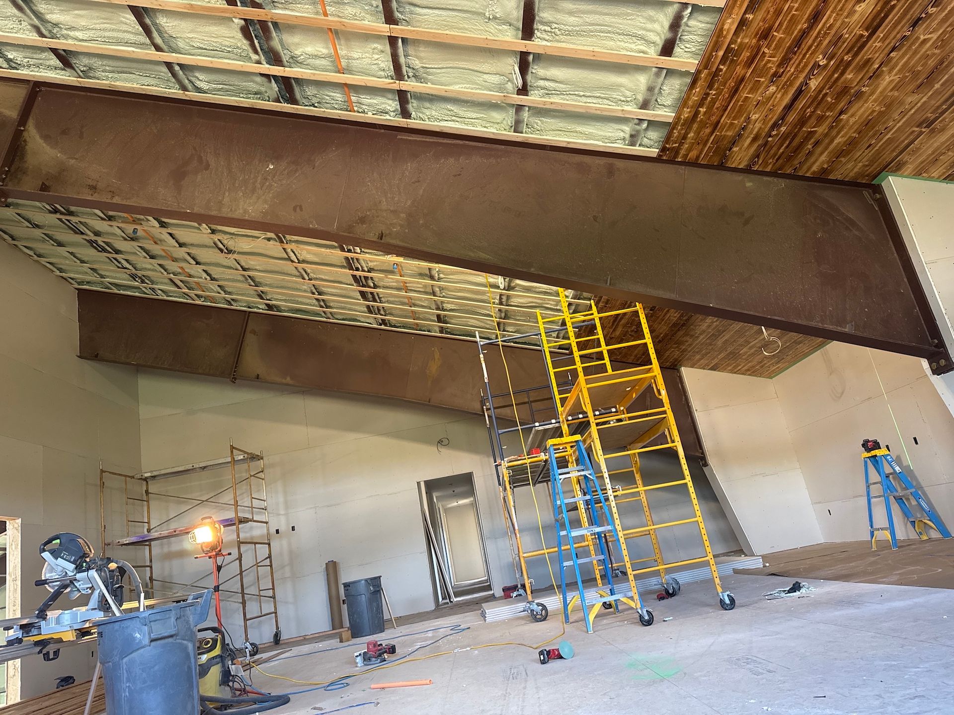 Workers inside a construction site with scaffolding, ladders, and exposed ceiling beams