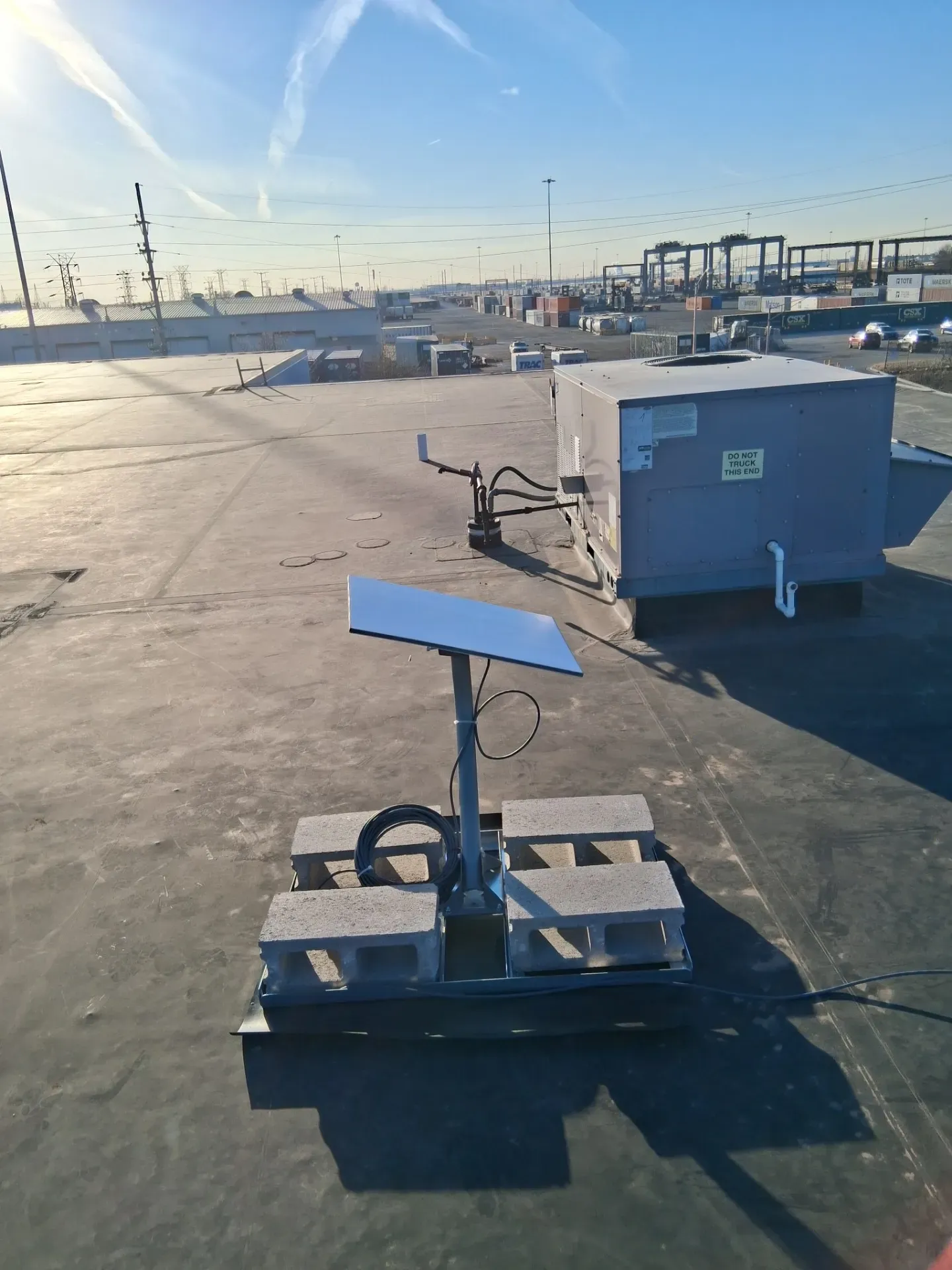 A Starlink satellite dish mounted on a metal frame weighted by concrete blocks on a flat, sunny rooftop.