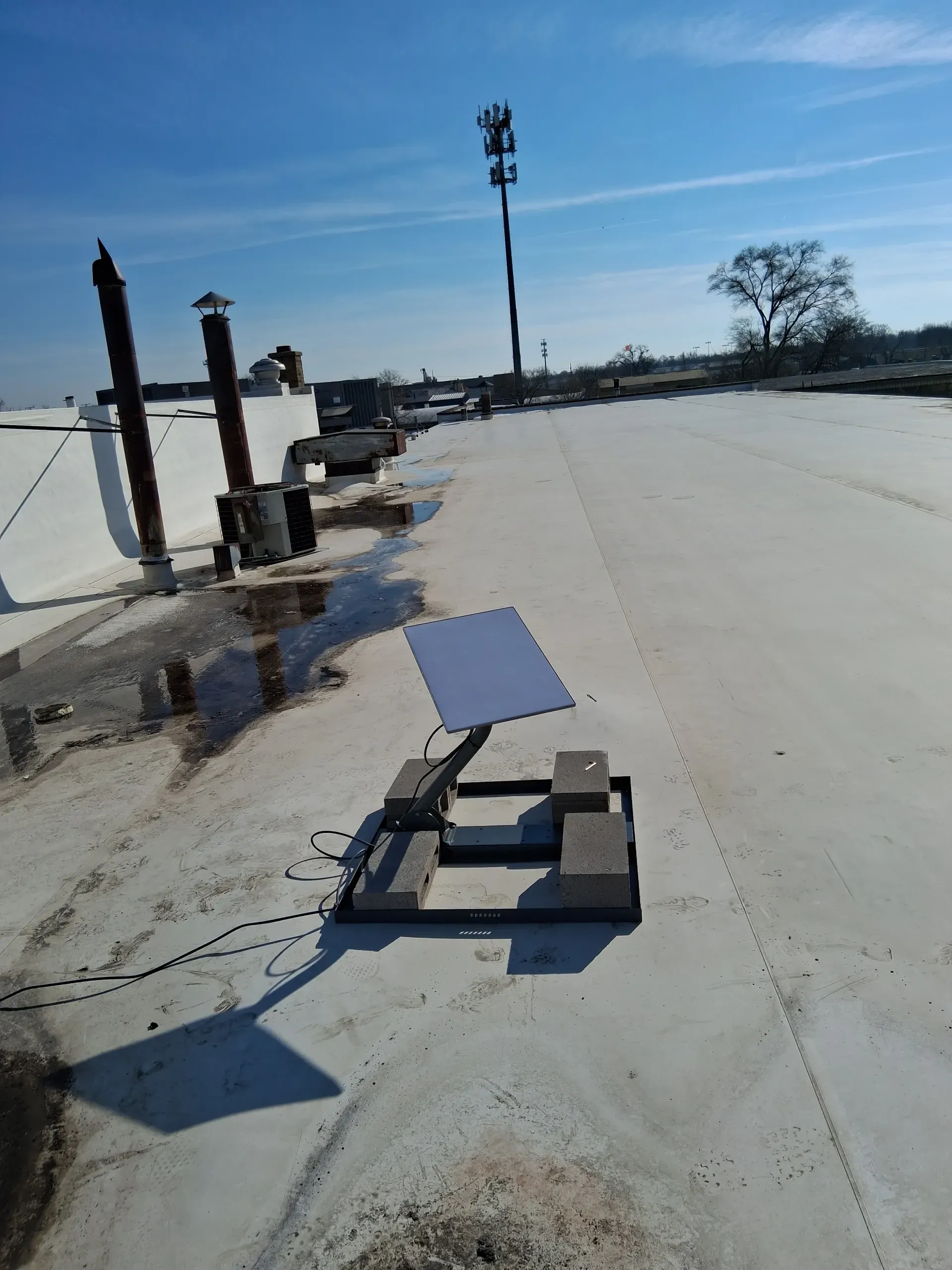 A Starlink satellite dish mounted on a frame with concrete blocks sits on a flat rooftop under a clear blue sky.