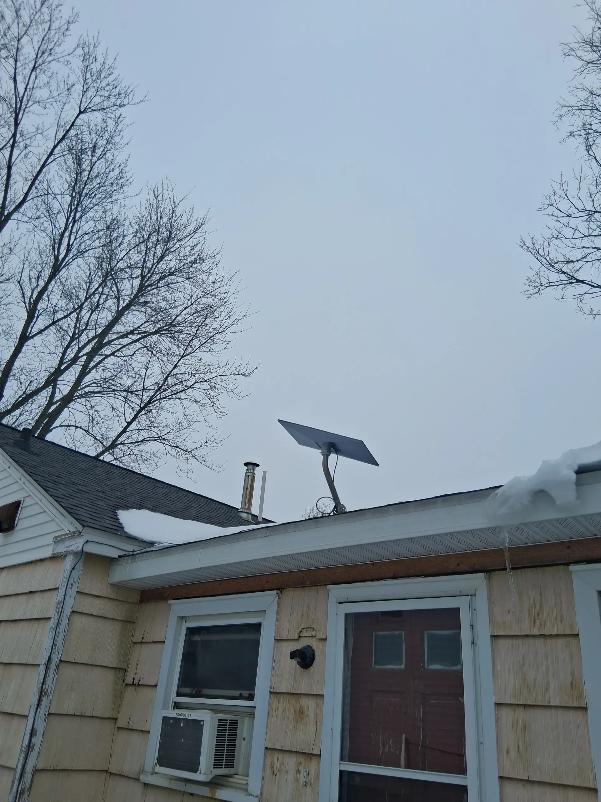 A Starlink satellite dish mounted on the roof of a beige house under a cloudy sky.
