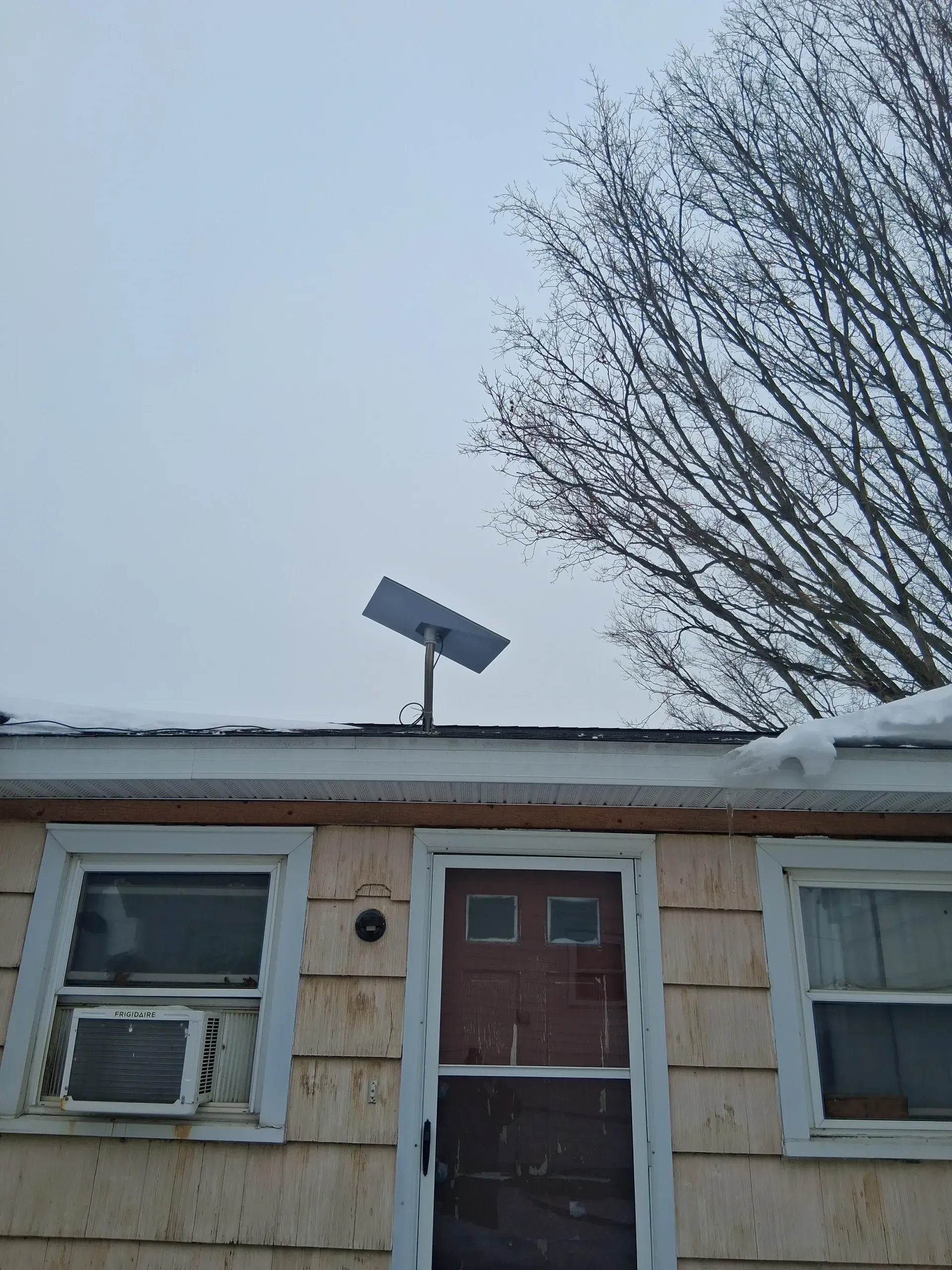 A Starlink satellite dish mounted on the roof of a beige-sided building with windows and a door, under a winter sky.