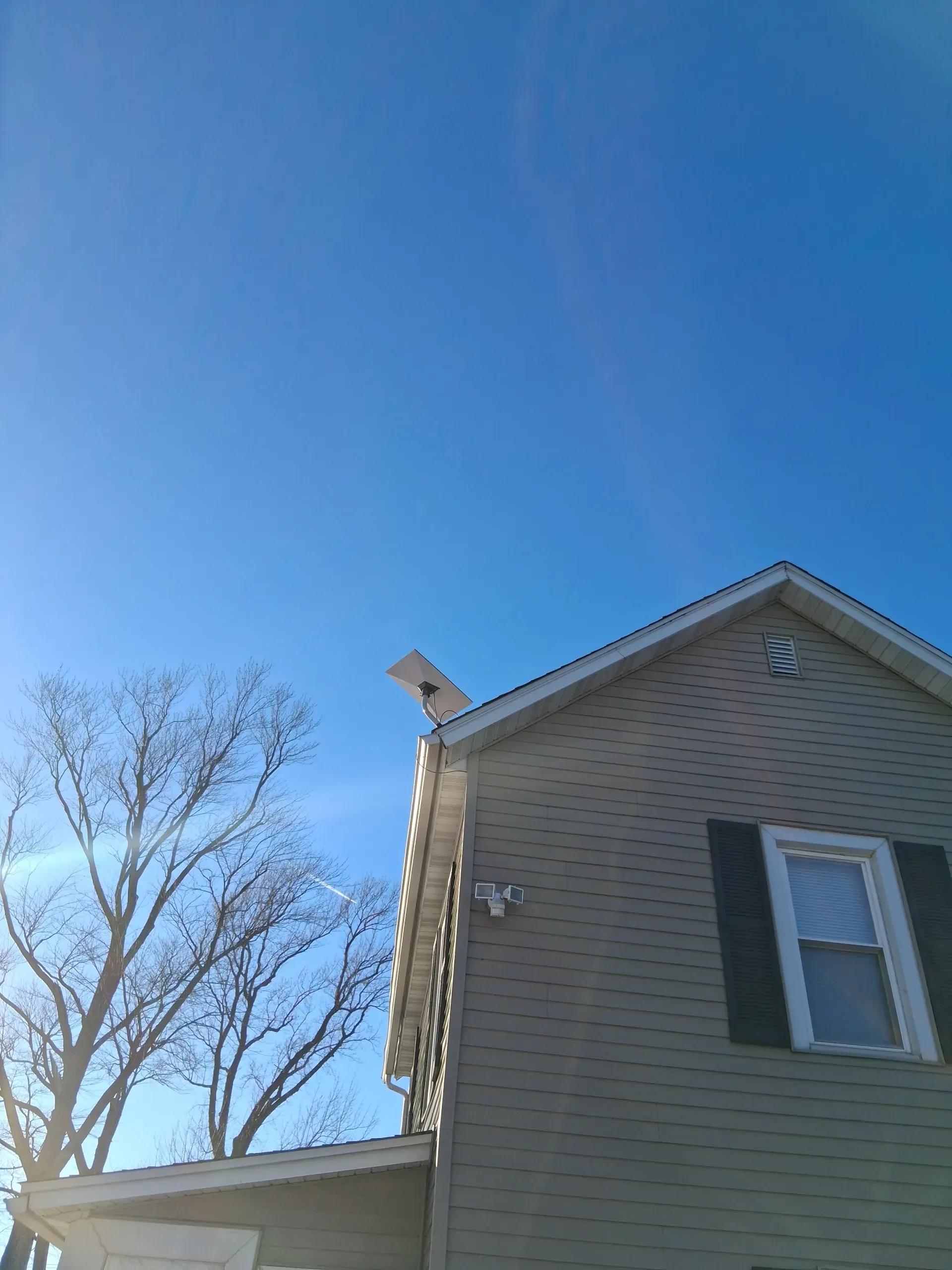 A light-colored house exterior against a clear blue sky, with a wireless internet antenna mounted on the roof eave.