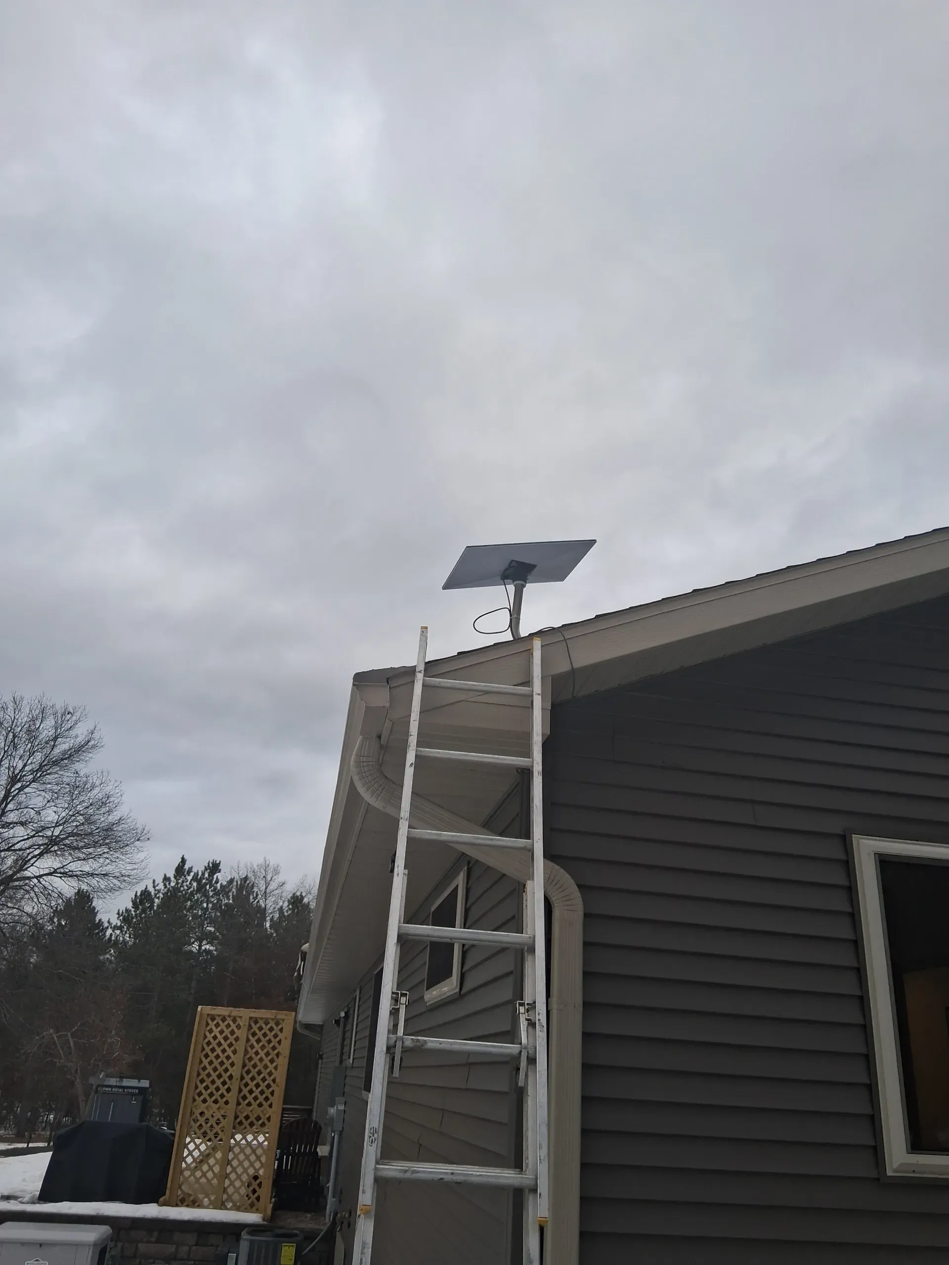A Starlink satellite dish mounted on the edge of a house roof, with an extension ladder leaning against the side.