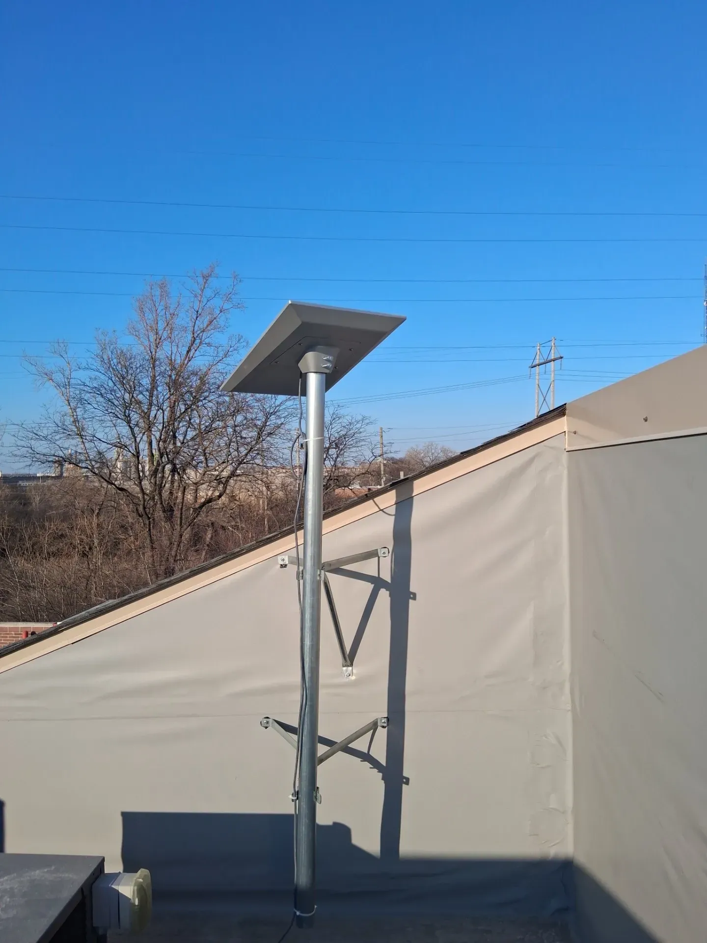 A Starlink satellite dish mounted on a vertical pole against a beige wall and a clear blue sky.