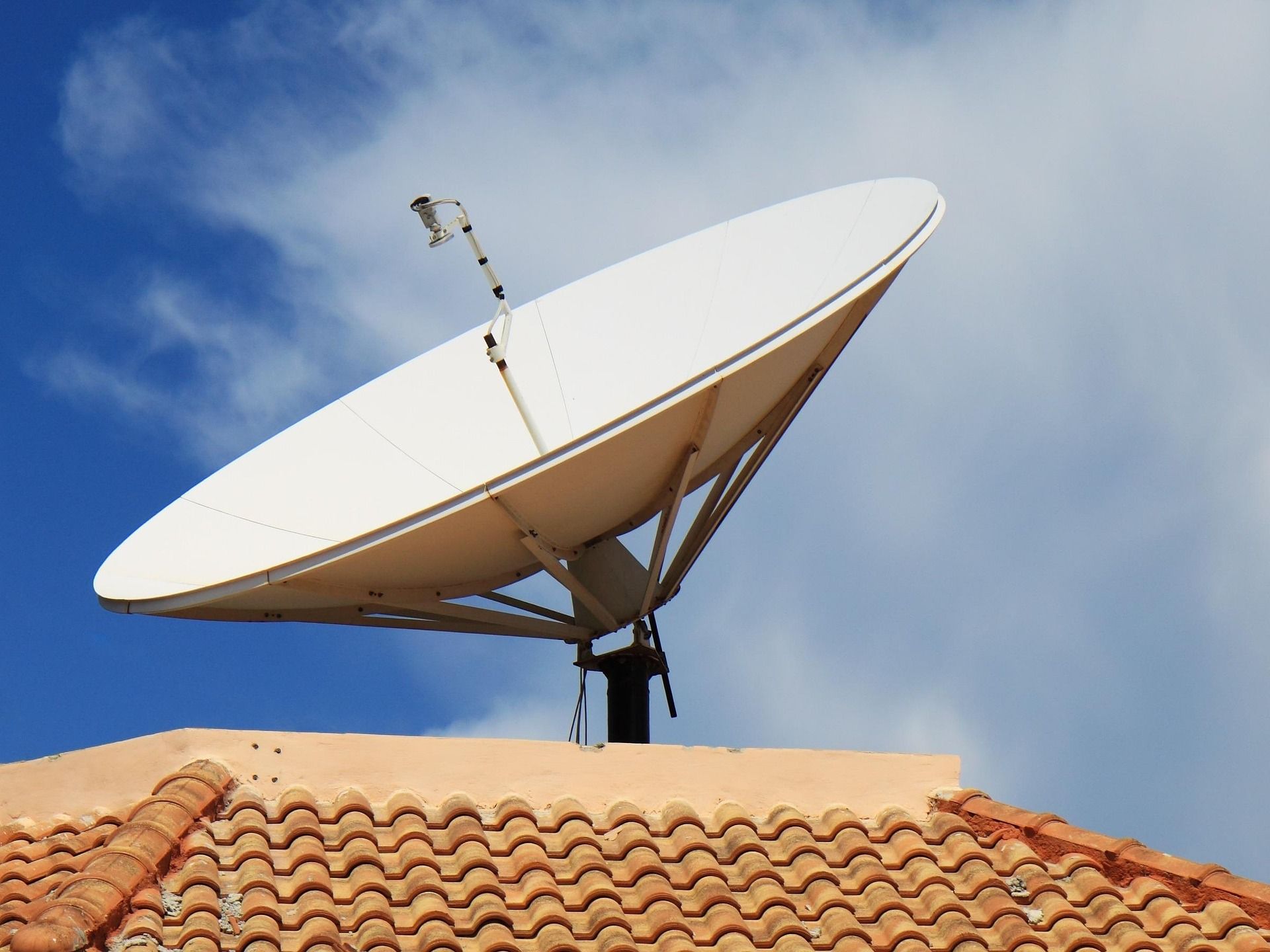 Satellite dish on a rooftop against a blue cloudy sky.