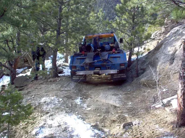 A blue truck is driving down a dirt road in the woods