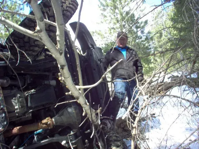 A man standing next to a crushed car in the woods