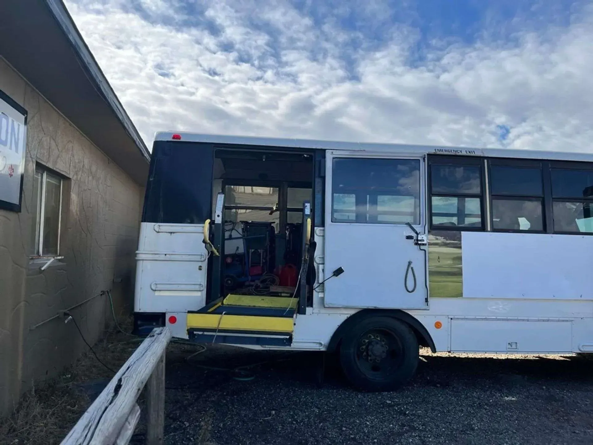 A white bus with the door open is parked in front of a building.
