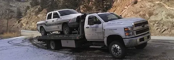 A tow truck is towing a pickup truck on a snowy road.