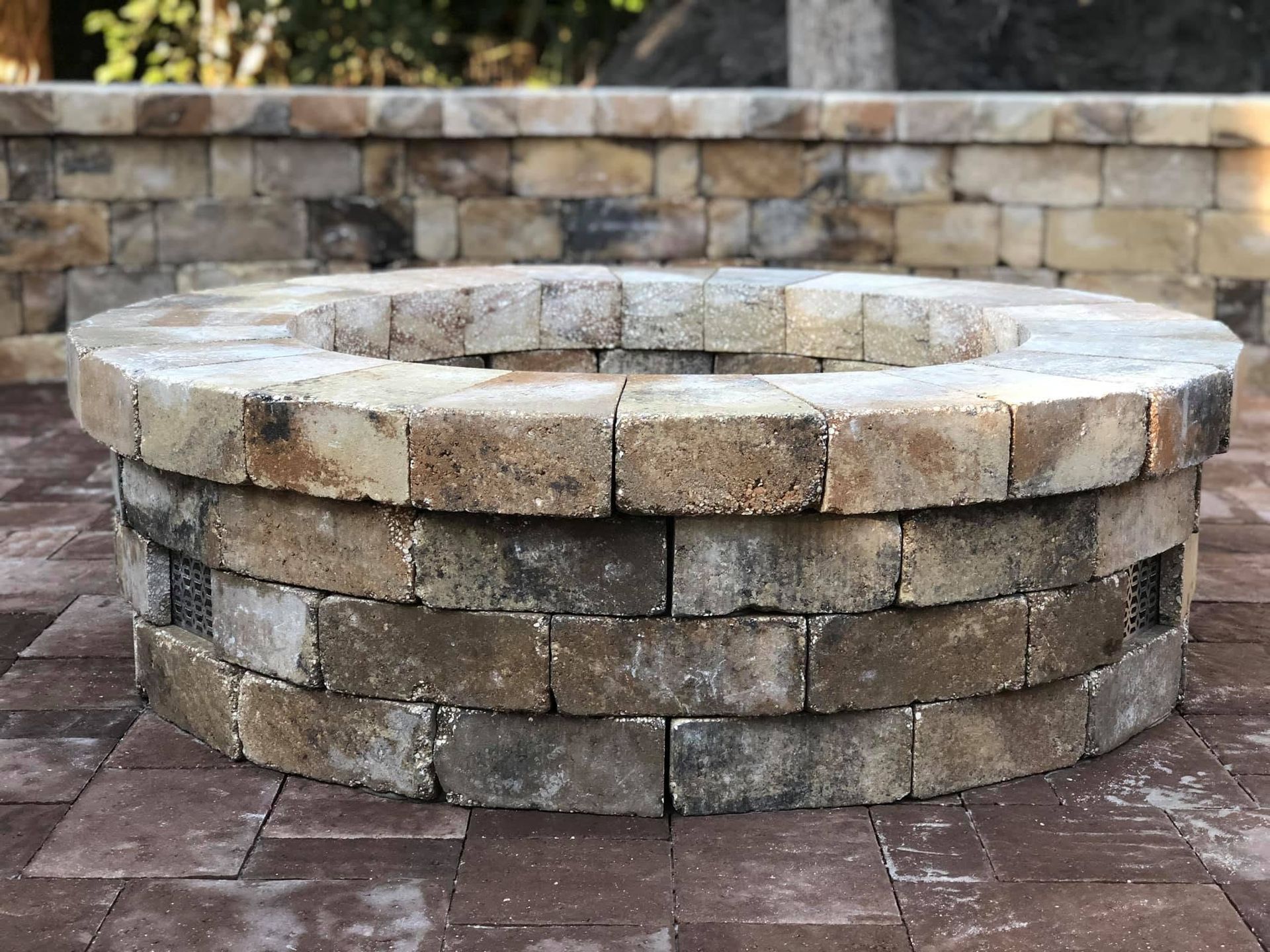 Stone fire pit in a patio courtyard with a circular brick border and stacked stone wall behind it