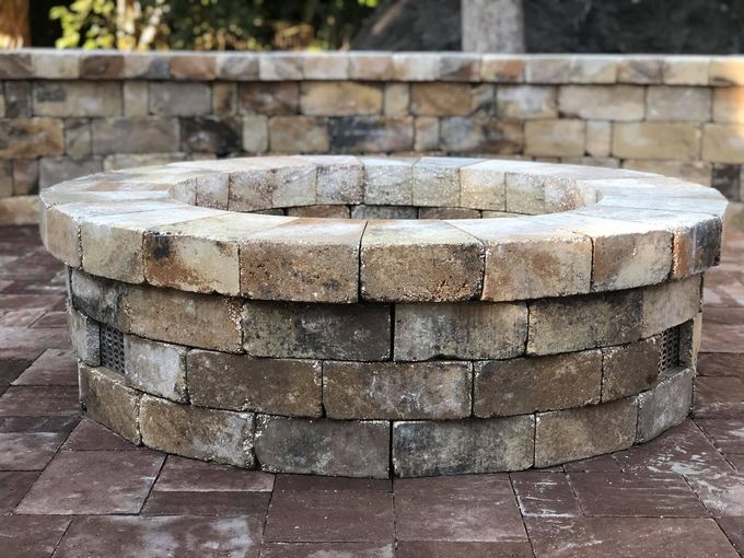 Stone fire pit in a paved patio with stacked stone wall backdrop