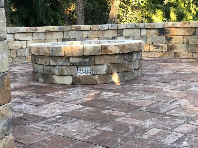 Stone fire pit on a paved patio beside a low stone retaining wall.