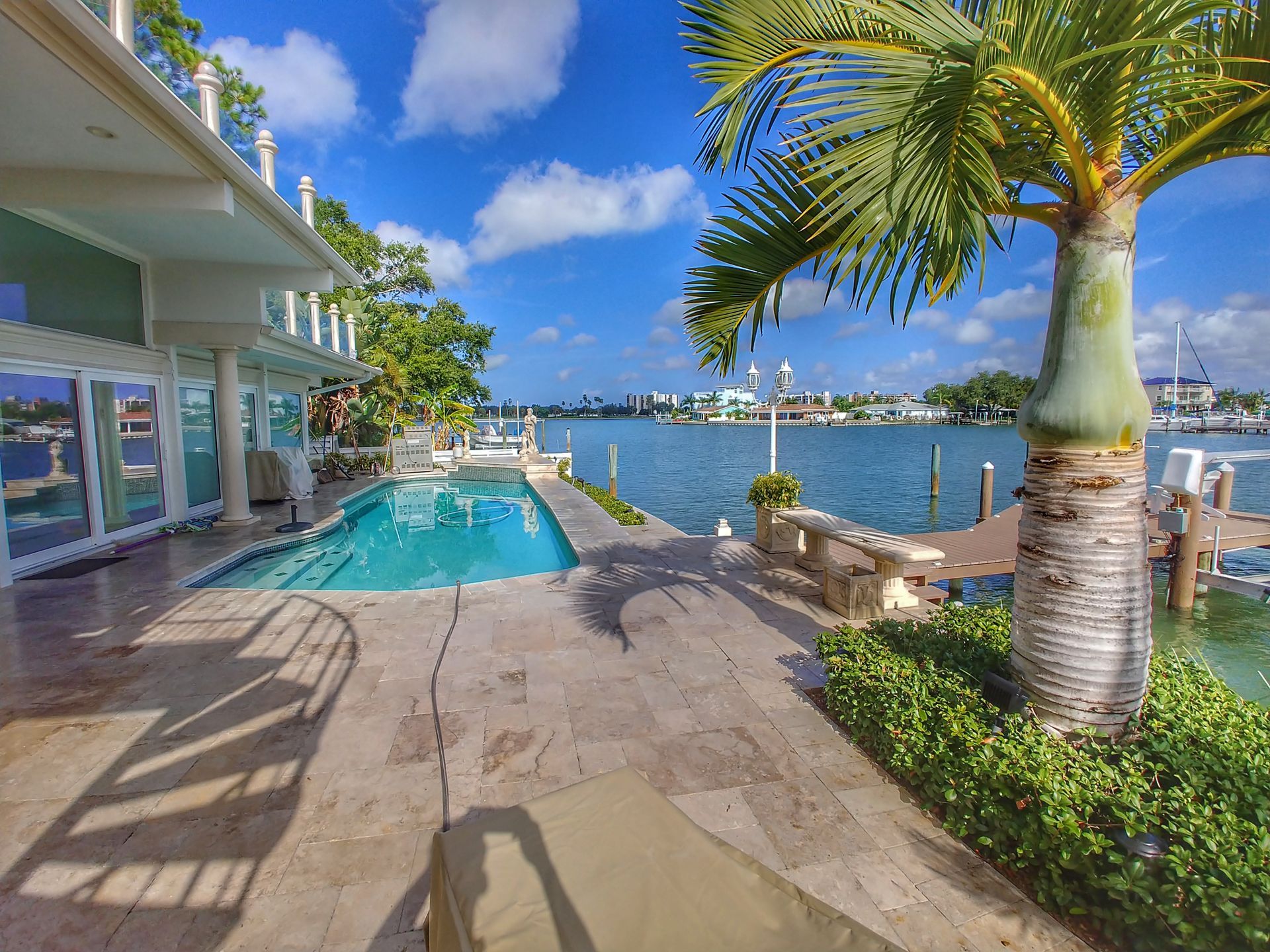 Waterfront patio with a pool, palm trees, and boats on a sunny tropical bay