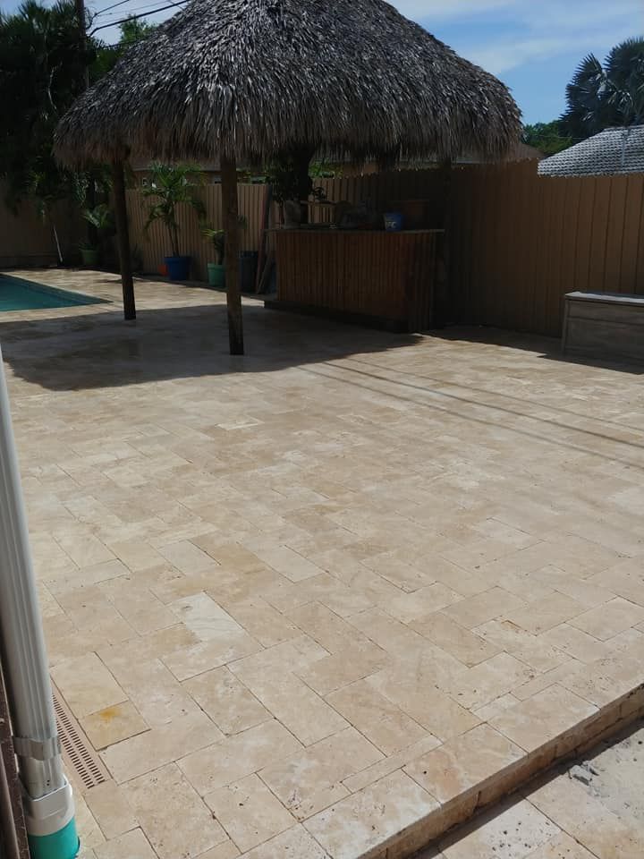 Sunlit stone patio with a thatched-roof hut and wooden fence