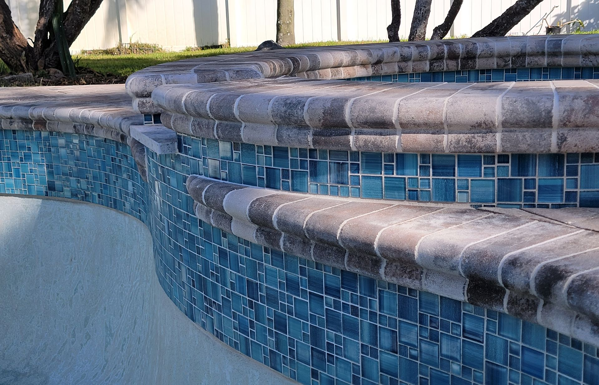 Blue tiled pool edge with curved stone coping and waterline tiles, showing a shallow pool wall.