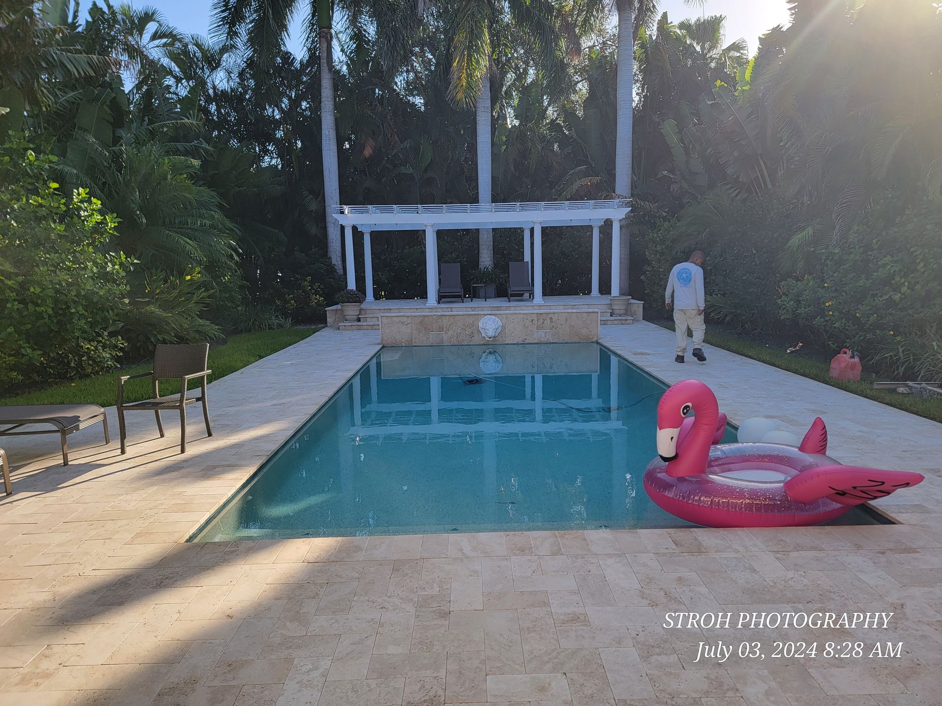 Backyard pool with pink flamingo float, lounge chairs, and a small pavilion in the background