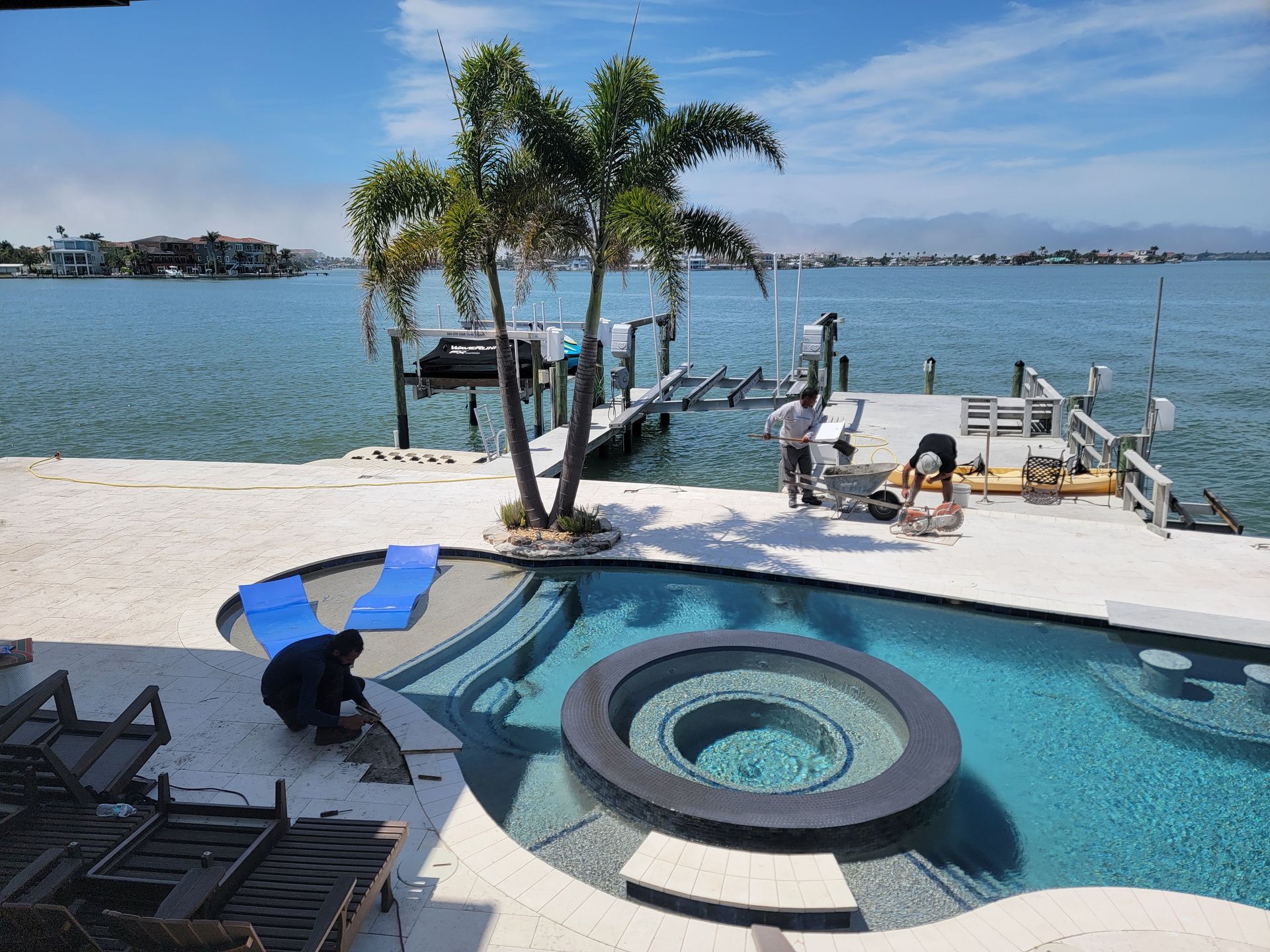 Backyard pool with palm trees, lounge chairs, and a dock on a calm waterfront