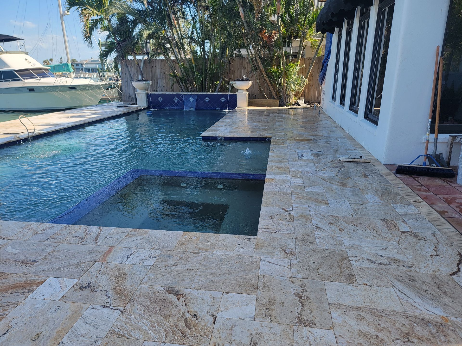 Poolside stone patio with blue swimming pool and steps beside a white house near a docked boat.