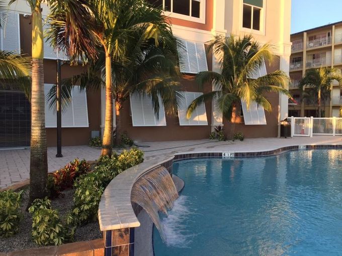 Palm-lined resort pool with a waterfall edge beside beige apartment buildings at sunset in Tampa, FL
