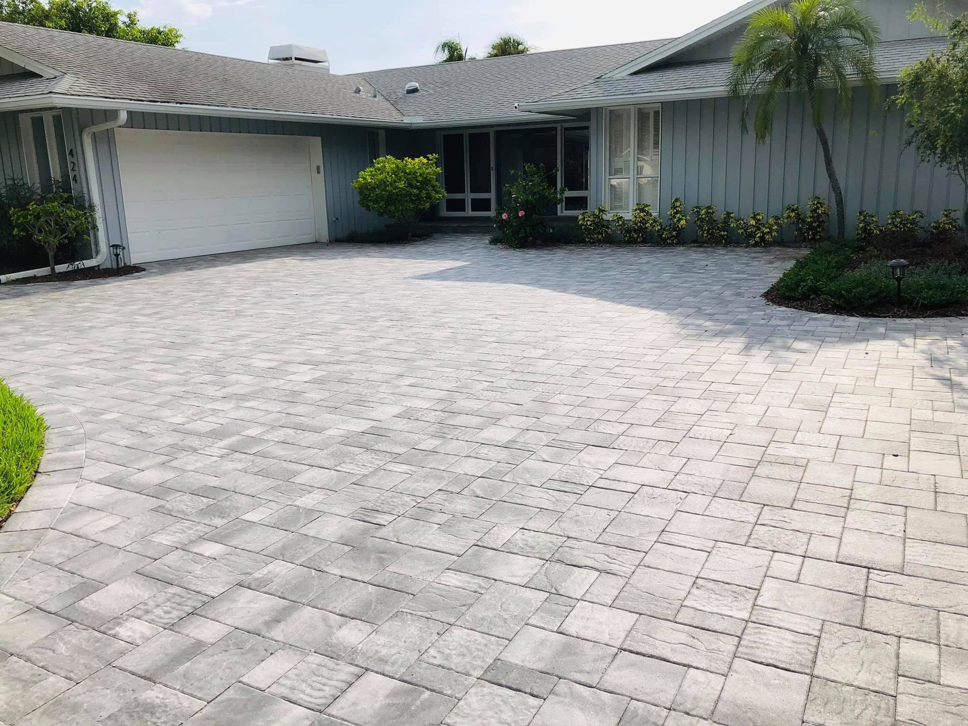 Single-story house with a large light-gray paver driveway and landscaped front yard