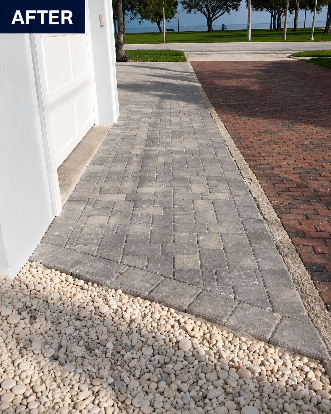 Paver walkway beside a white building, bordered by gravel and a brick path near a grassy waterfront.