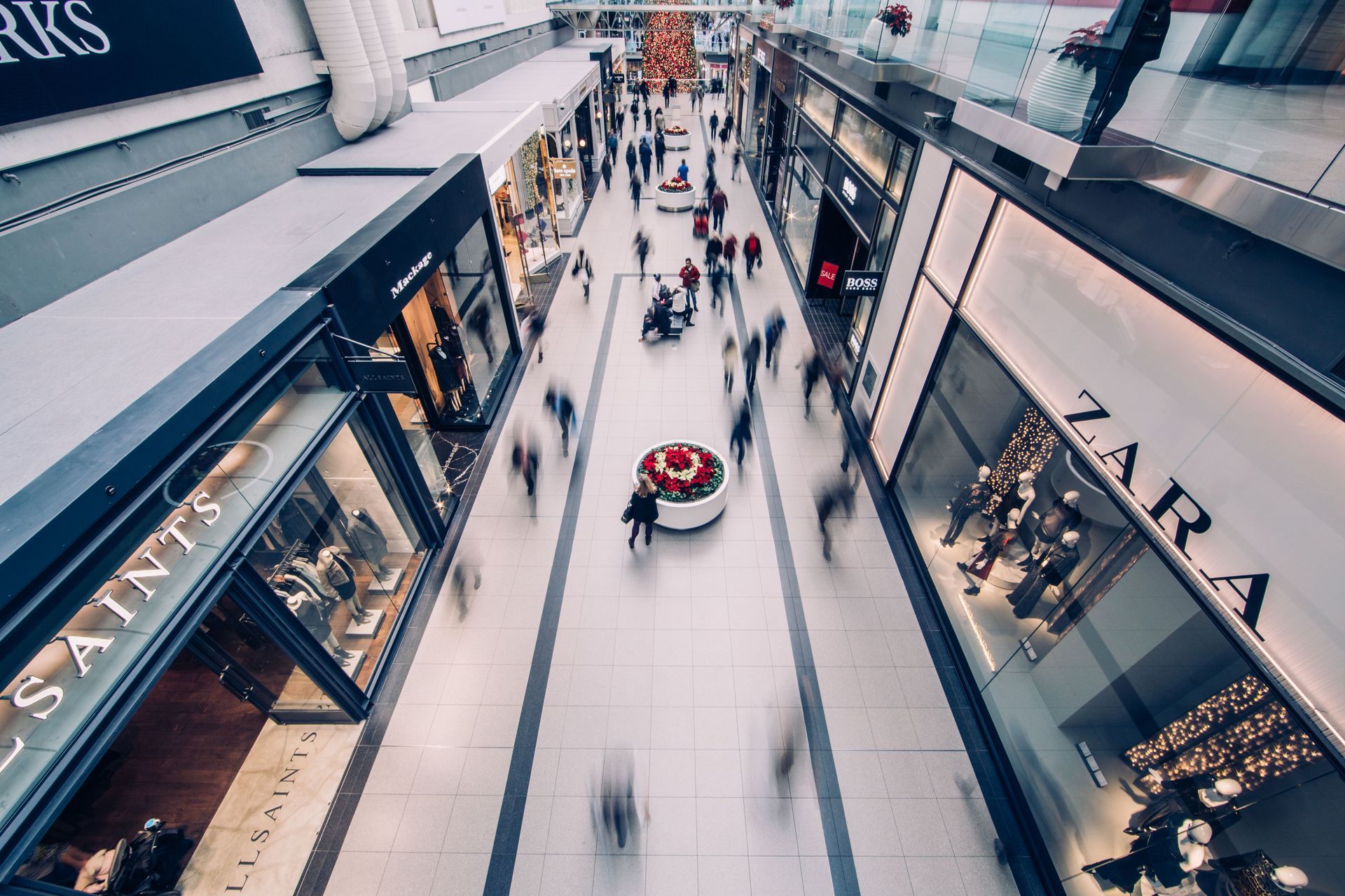 Indoor shopping mall corridor with clothing stores and a small red ride in the center