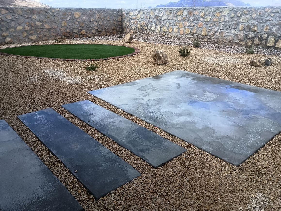 A stone wall surrounds a gravel area with a grassy area in the middle