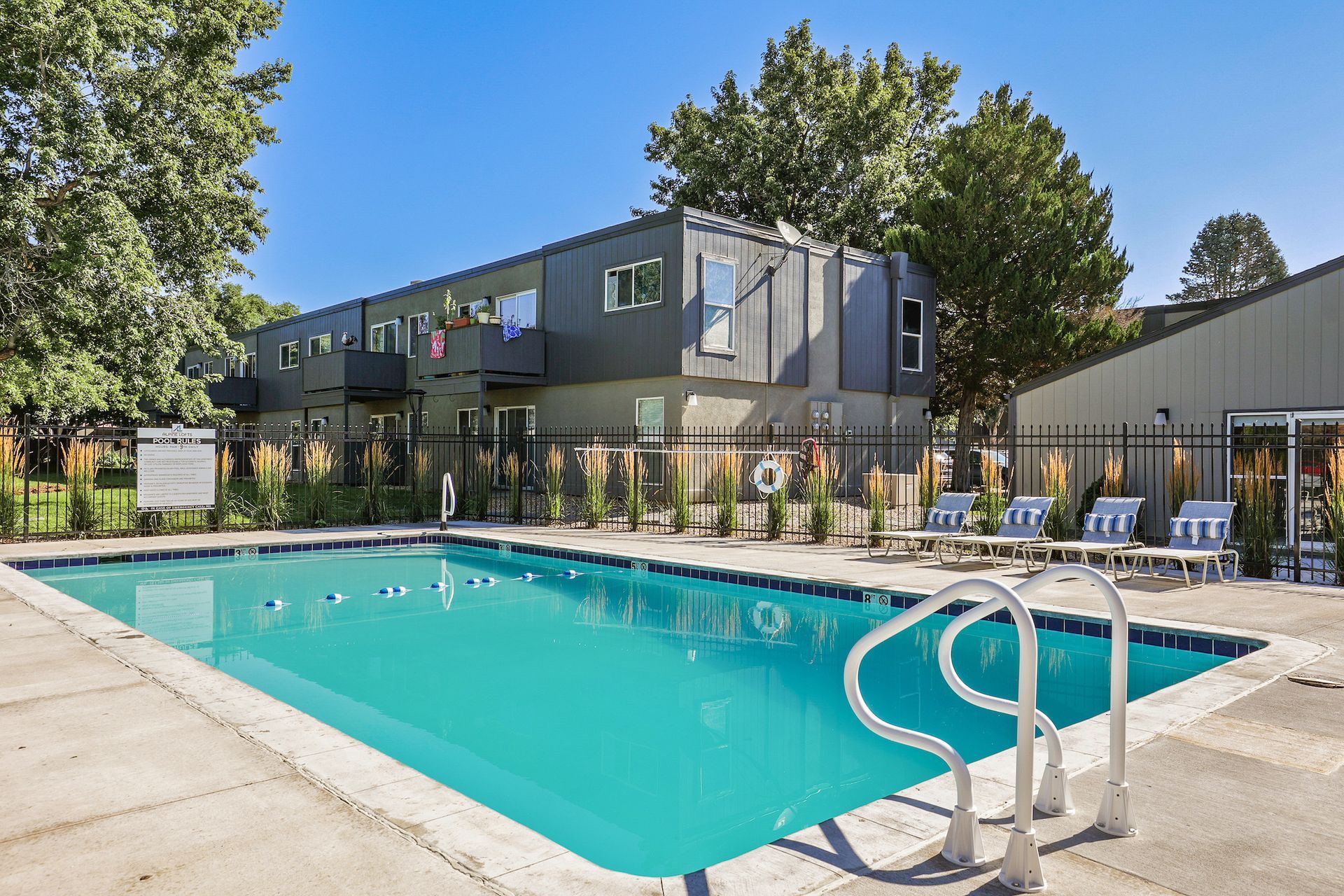 A swimming pool with lounge chairs on a concrete deck in front of a modern apartment building.