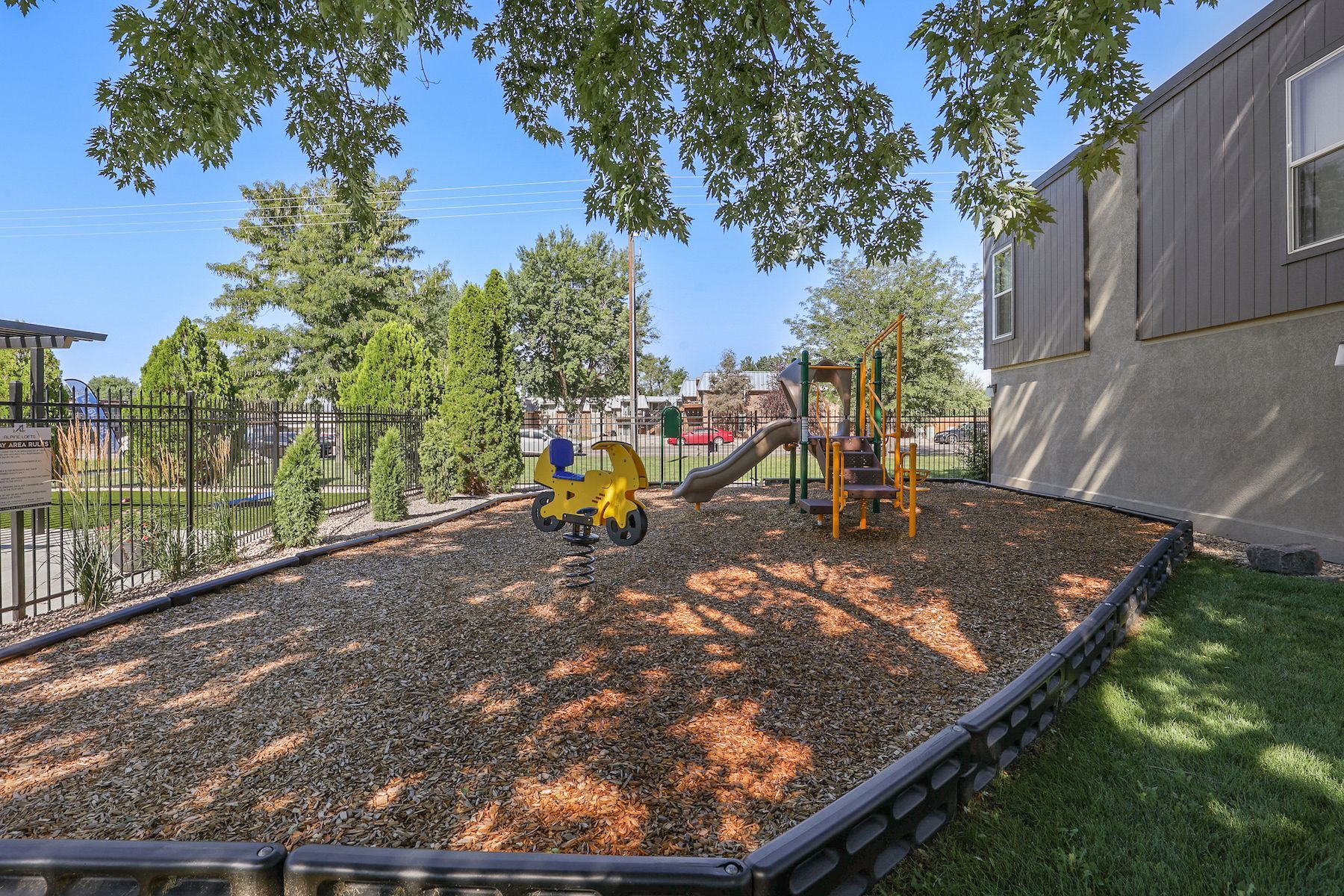 A small playground area with wood mulch, a yellow spring rider, and a slide set against a building.