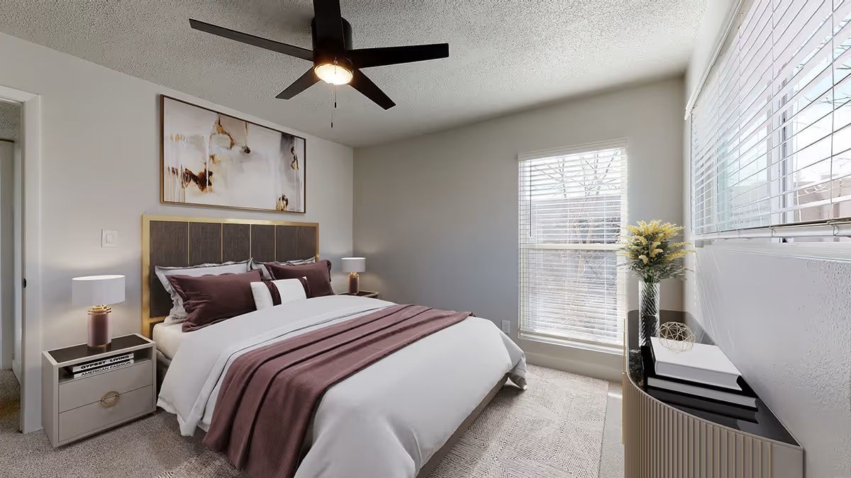 A bedroom featuring a bed with a dark headboard, white and plum bedding, a ceiling fan, and a window with blinds.